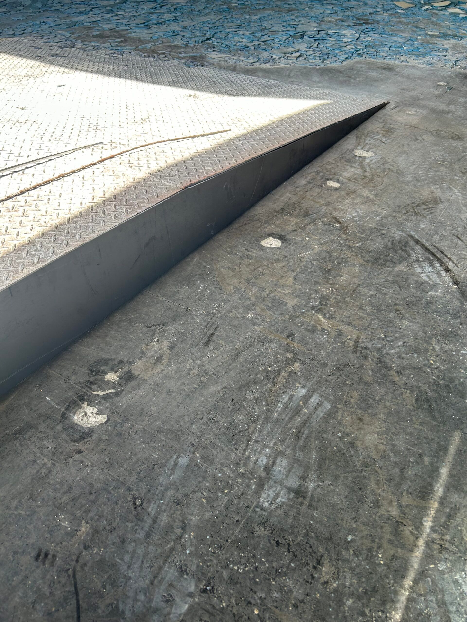 Concrete curb ramp with a dark asphalt edge and white textured paving beside it.