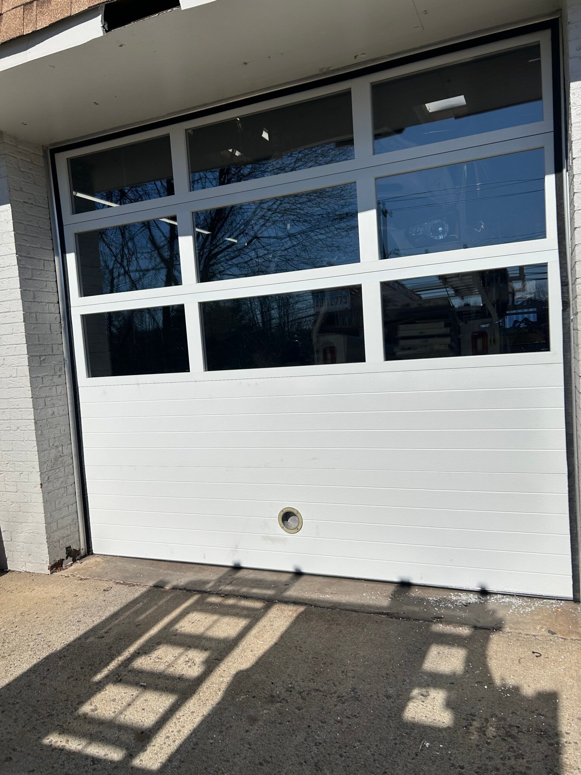 White garage-style door with windows in a building exterior, sunlight casting shadows on the pavement.