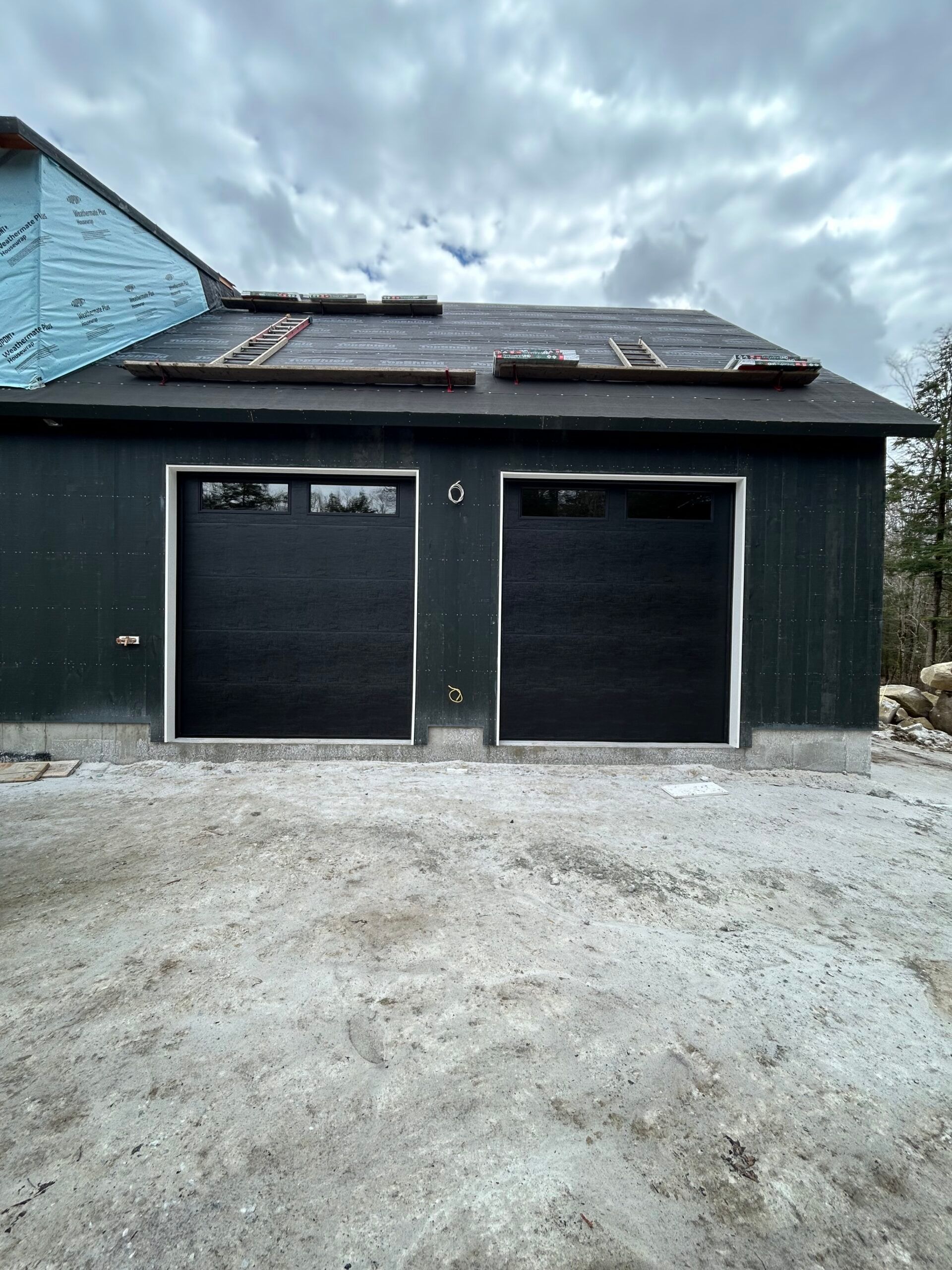 Two-car garage with dark doors, gravel driveway, and cloudy sky overhead