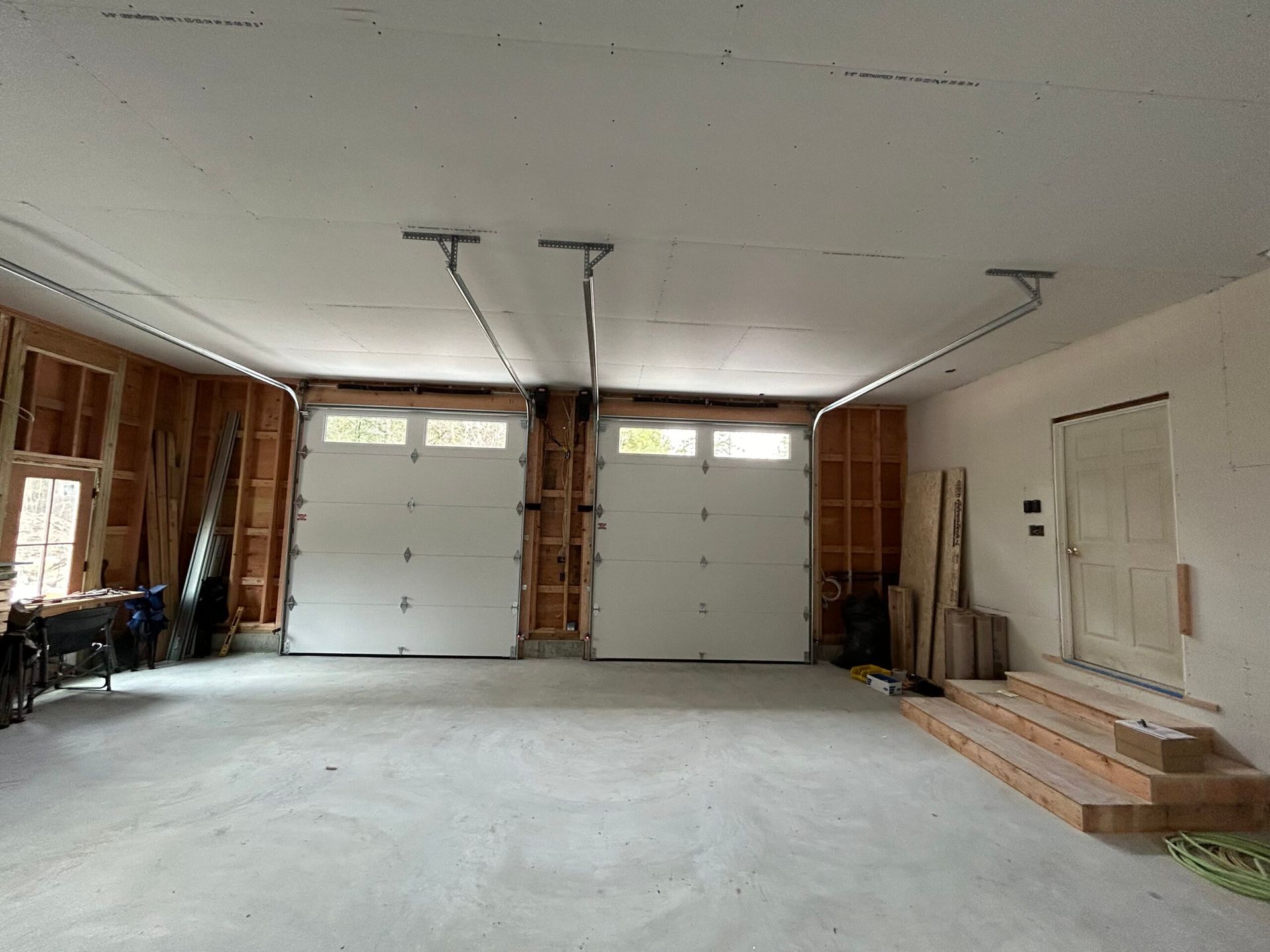 Empty garage interior with two white doors, unfinished walls, and concrete floor