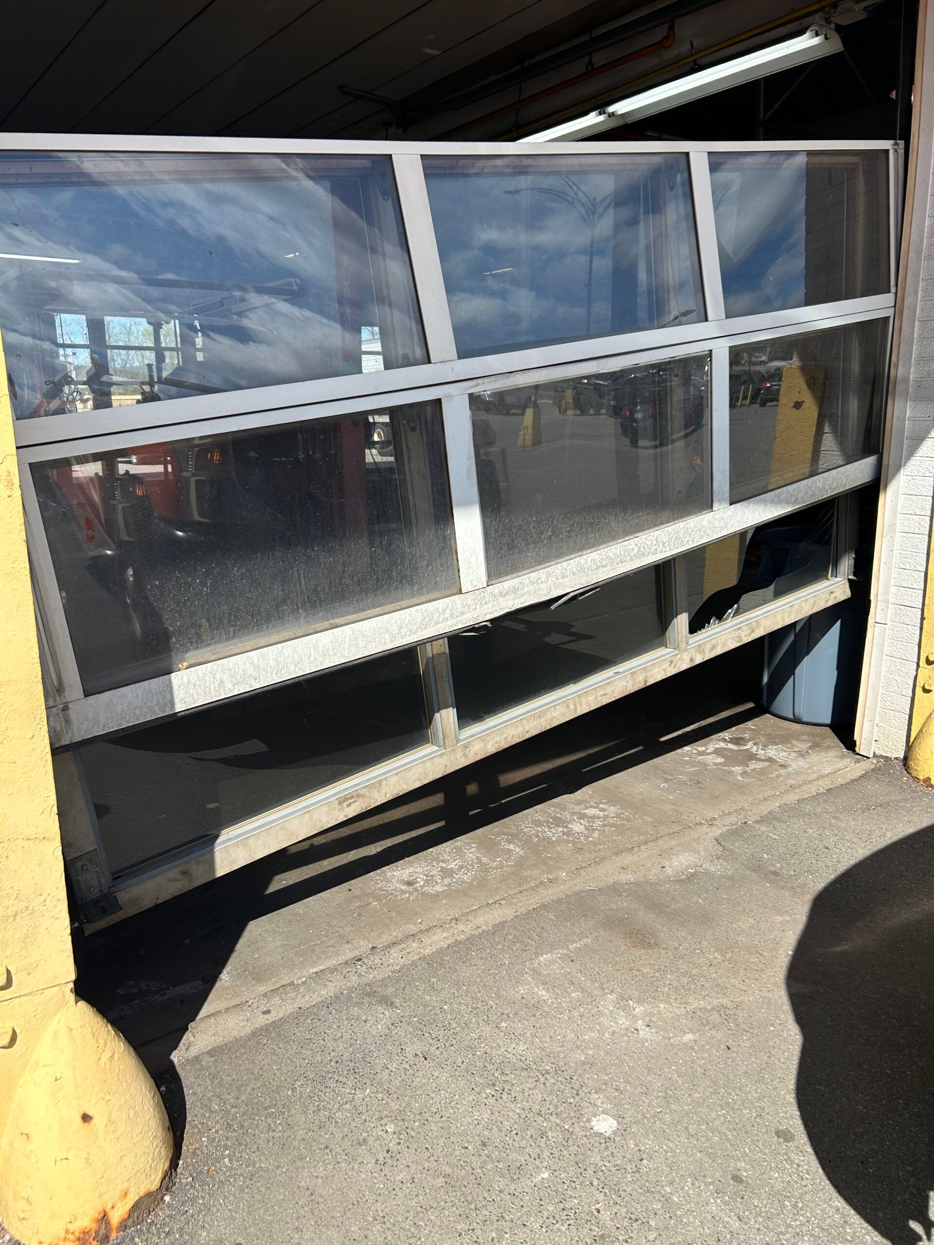 Damaged storefront window with broken lower panel and reflective glass under a covered walkway