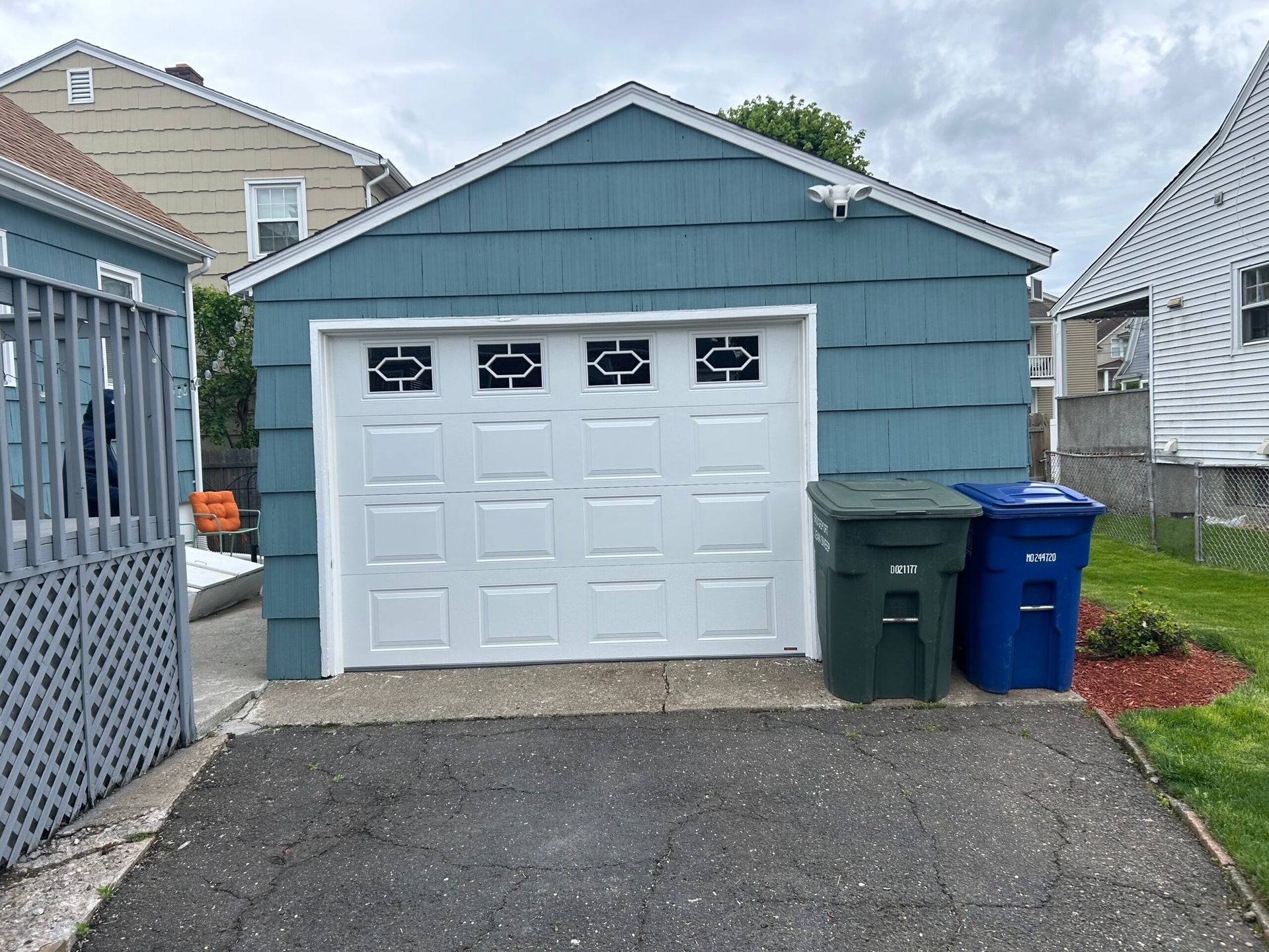 Blue detached garage with a white door, driveway, and two trash bins beside it