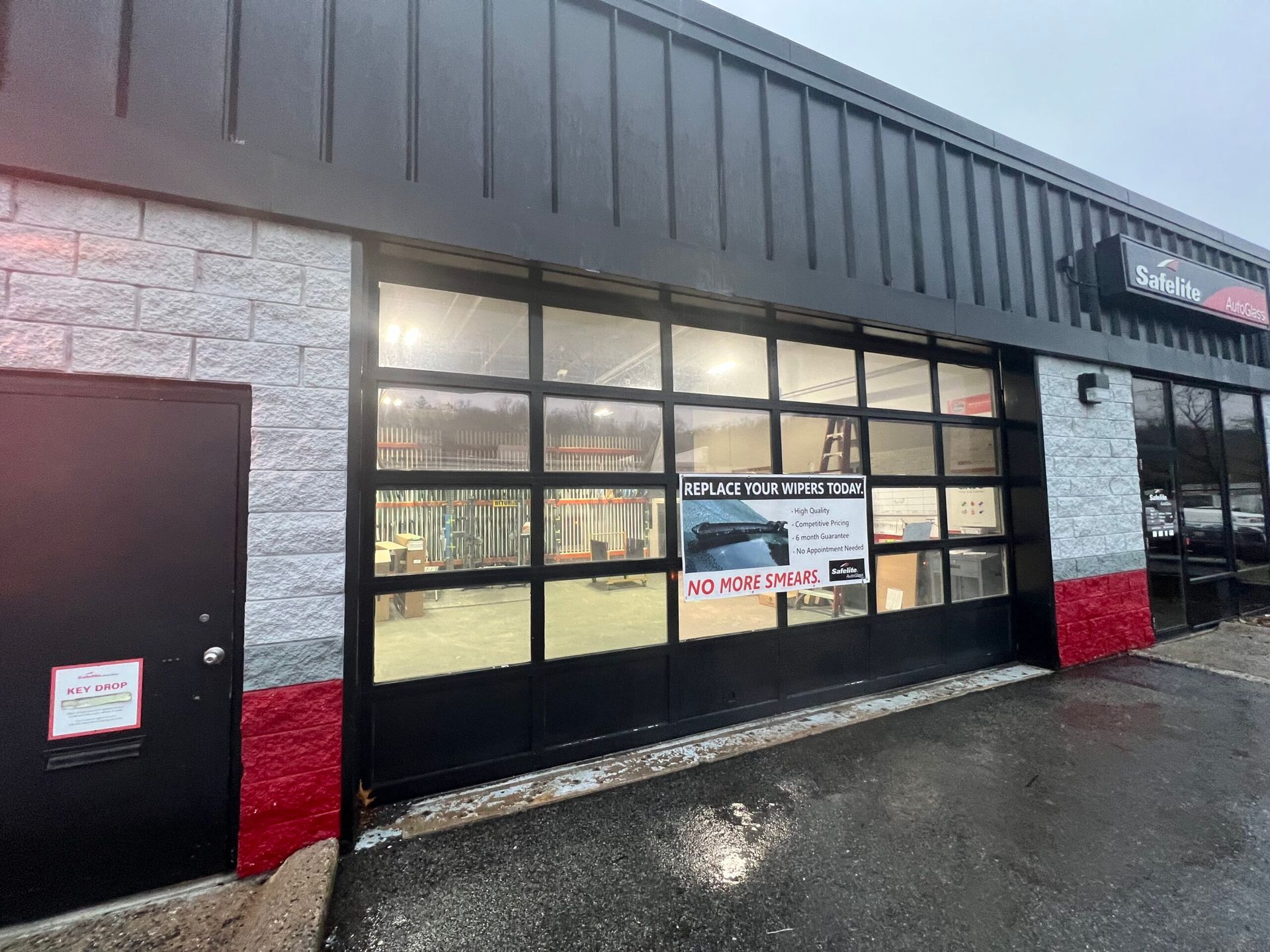 Storefront with black garage-style windows, red lower trim, and a wet pavement outside.