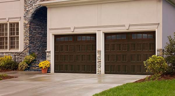 Two-car garage with brown doors on a suburban house, bordered by shrubs and flowers.
