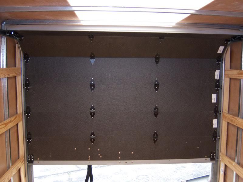 Inside an open moving truck, a large upright mattress or panel is secured against the wall.