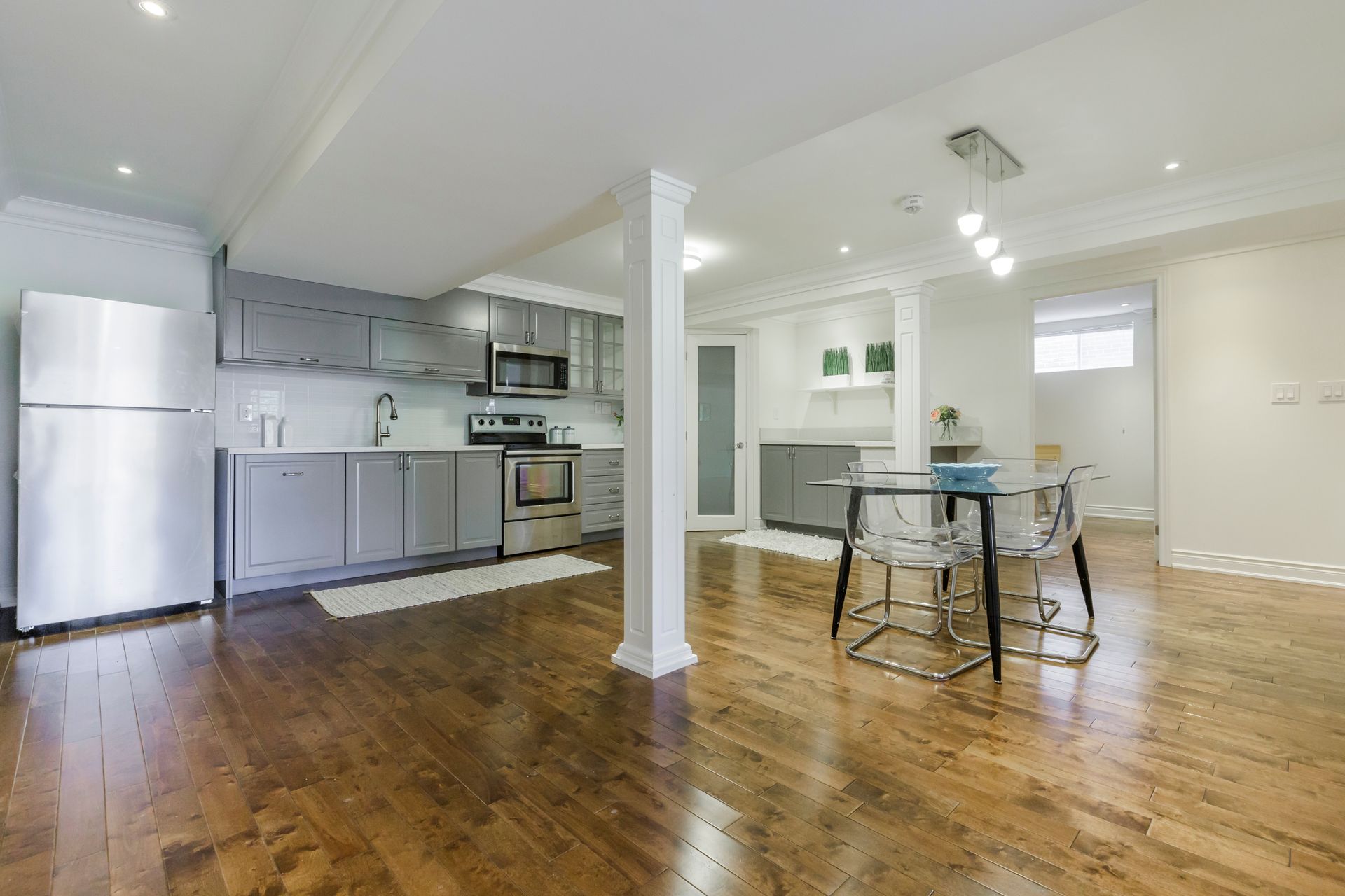 Modern basement kitchen with stainless steel appliances, gray cabinets, and a dining table.