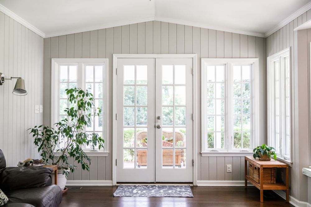 Sunroom with French doors, windows, gray paneling, and indoor plants.