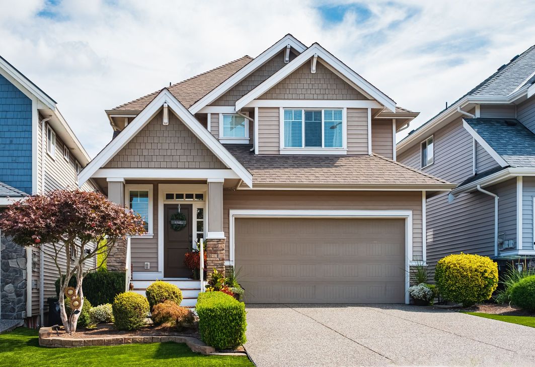 Brown two-story house with garage, shrubs, and blue sky.