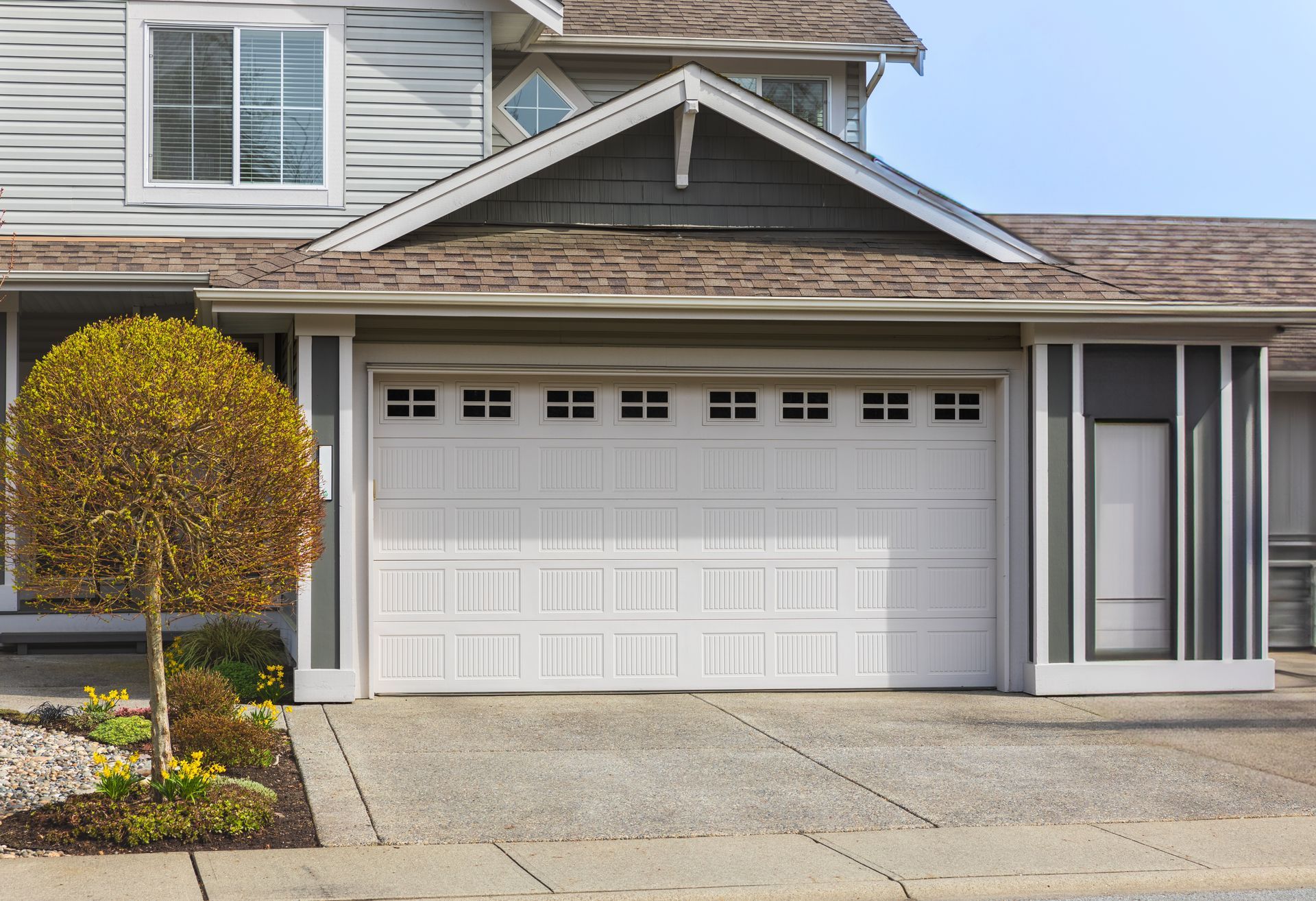 White garage door on a house with a small tree in front.