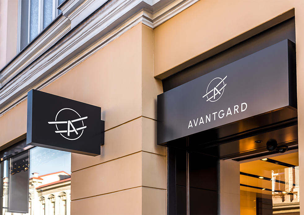 Výloha s černým nápisem „AVANTGARD“ na béžové fasádě budovy.