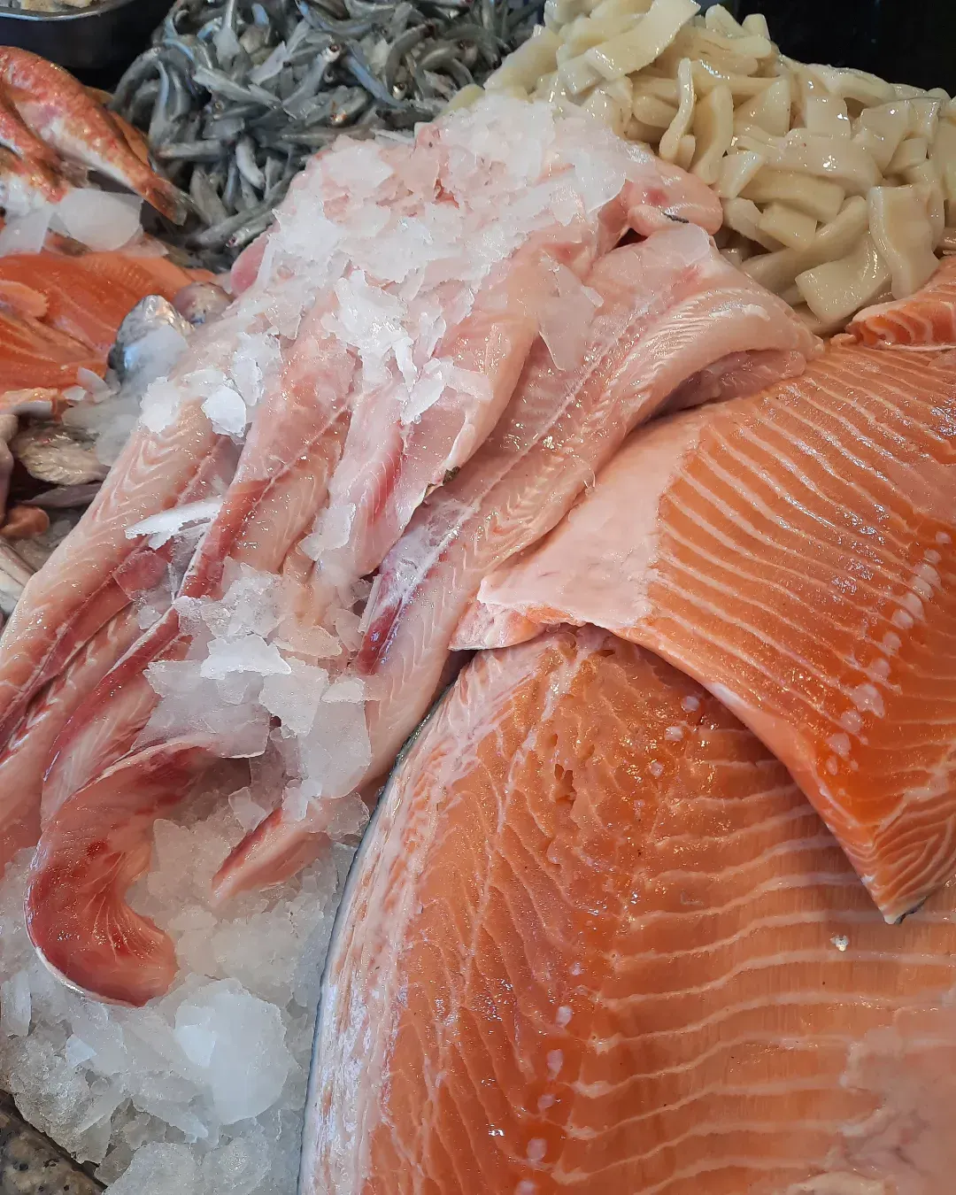 Surtido de mariscos sobre hielo, incluyendo filetes de salmón, calamares y camarones en un mostrador de mercado.