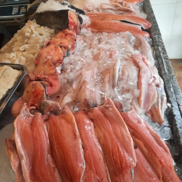 Exhibición de mariscos con filas de filetes de pescado rojo, camarones y otros pescados congelados sobre hielo.
