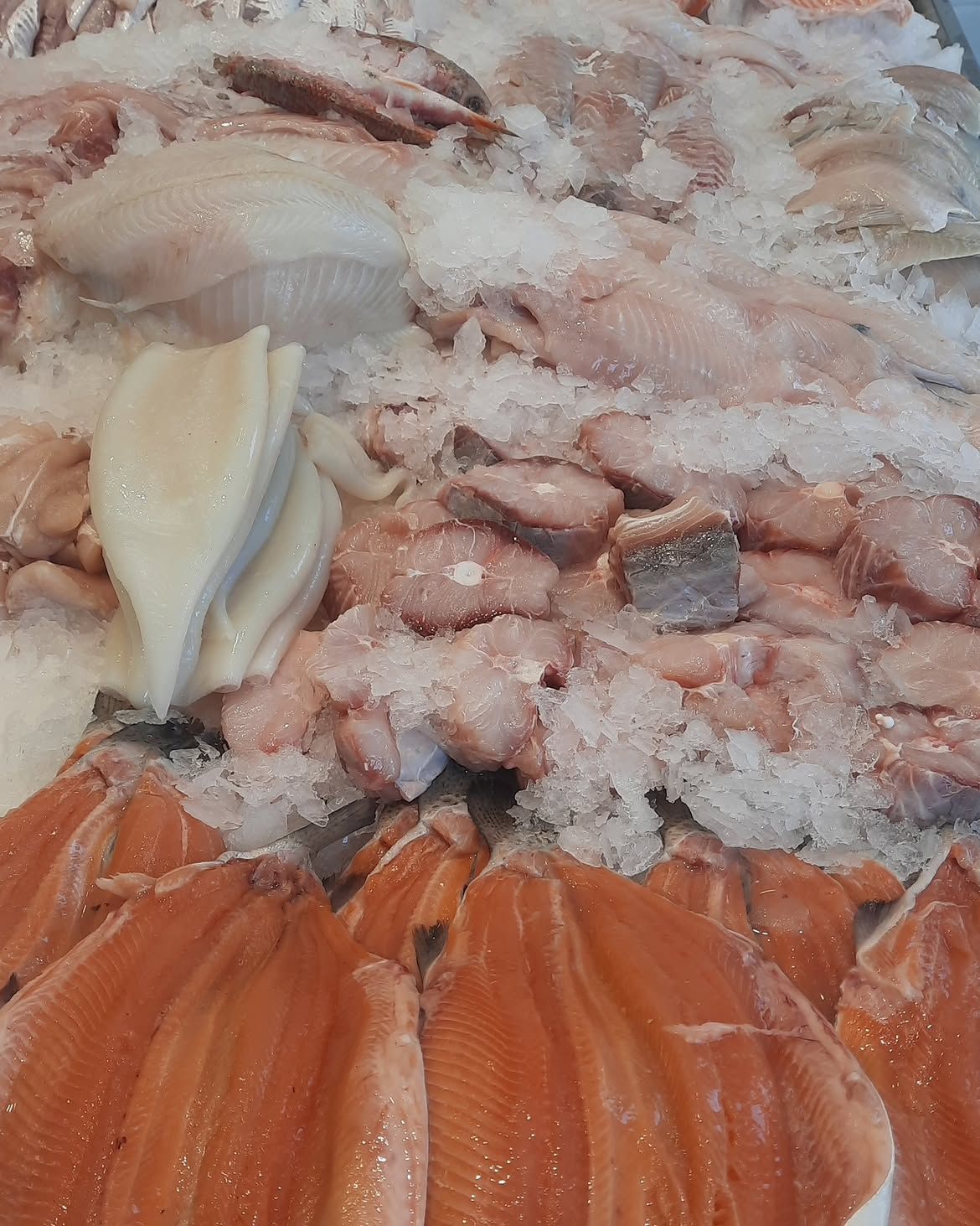 Surtido de mariscos y filetes de pescado sobre hielo, incluyendo trozos de salmón anaranjado y carne de marisco blanco.