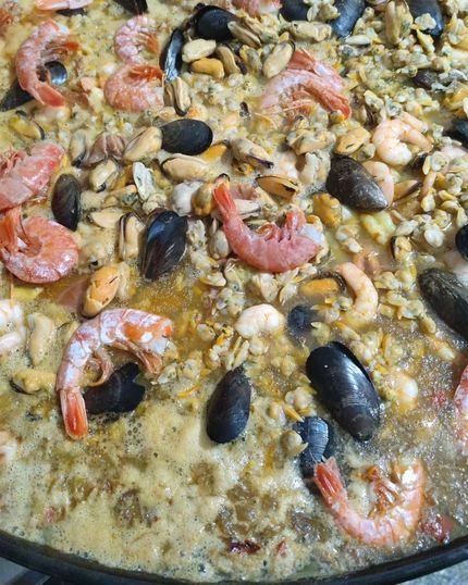 Paella de marisco con gambas, mejillones, arroz y verduras en una sartén.