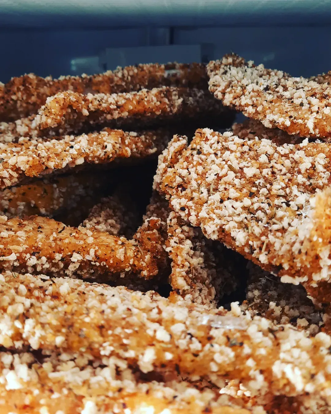 Primer plano de barritas de cereales recubiertas de sésamo apiladas en un recipiente azul.