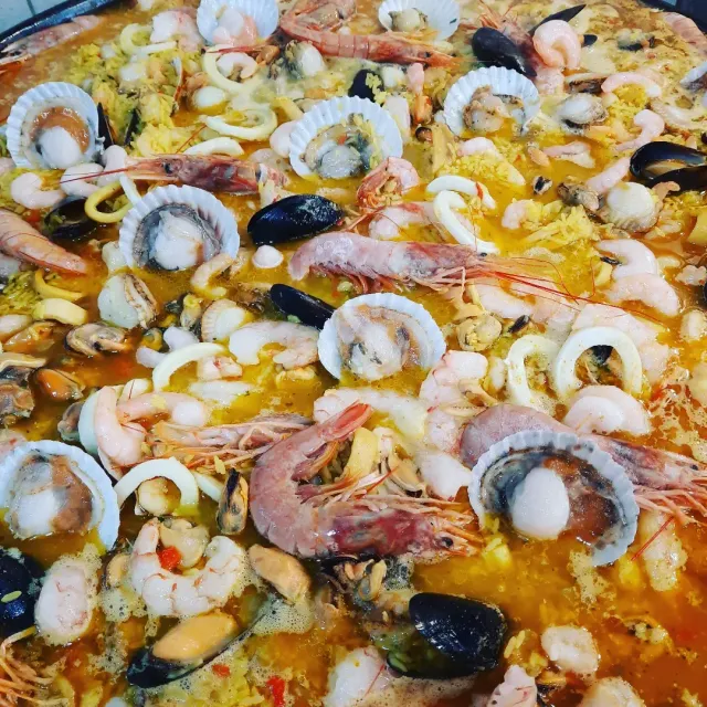 Paella de marisco con gambas, mejillones y calamares en un plato de arroz dorado.