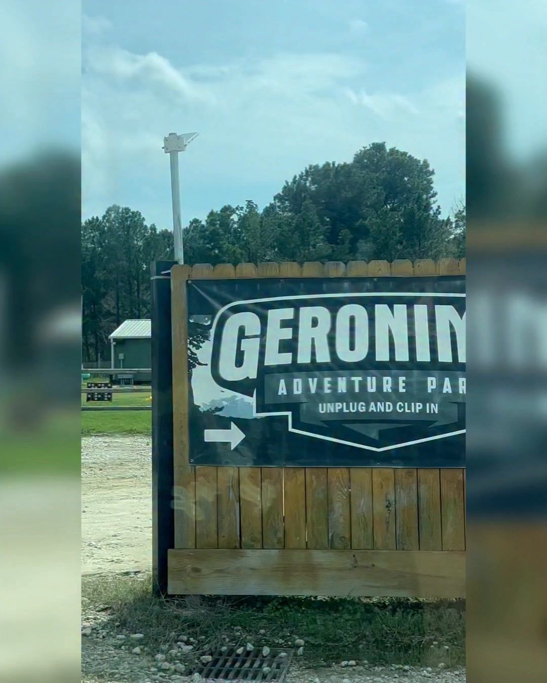 Geronimo Adventure Park sign on a wooden fence with trees and cloudy sky behind it