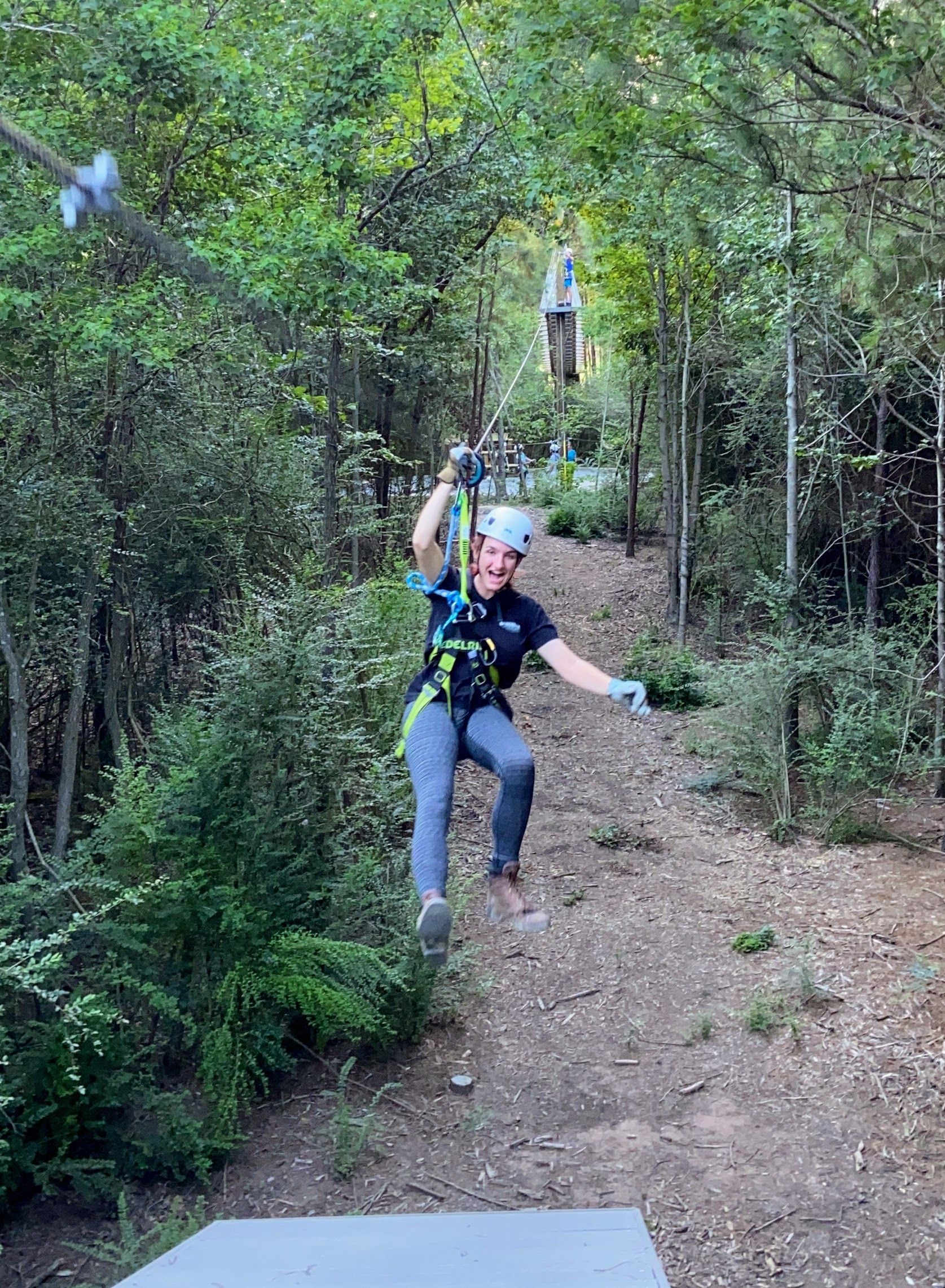 Person zip-lining through a wooded trail, wearing a helmet and harness