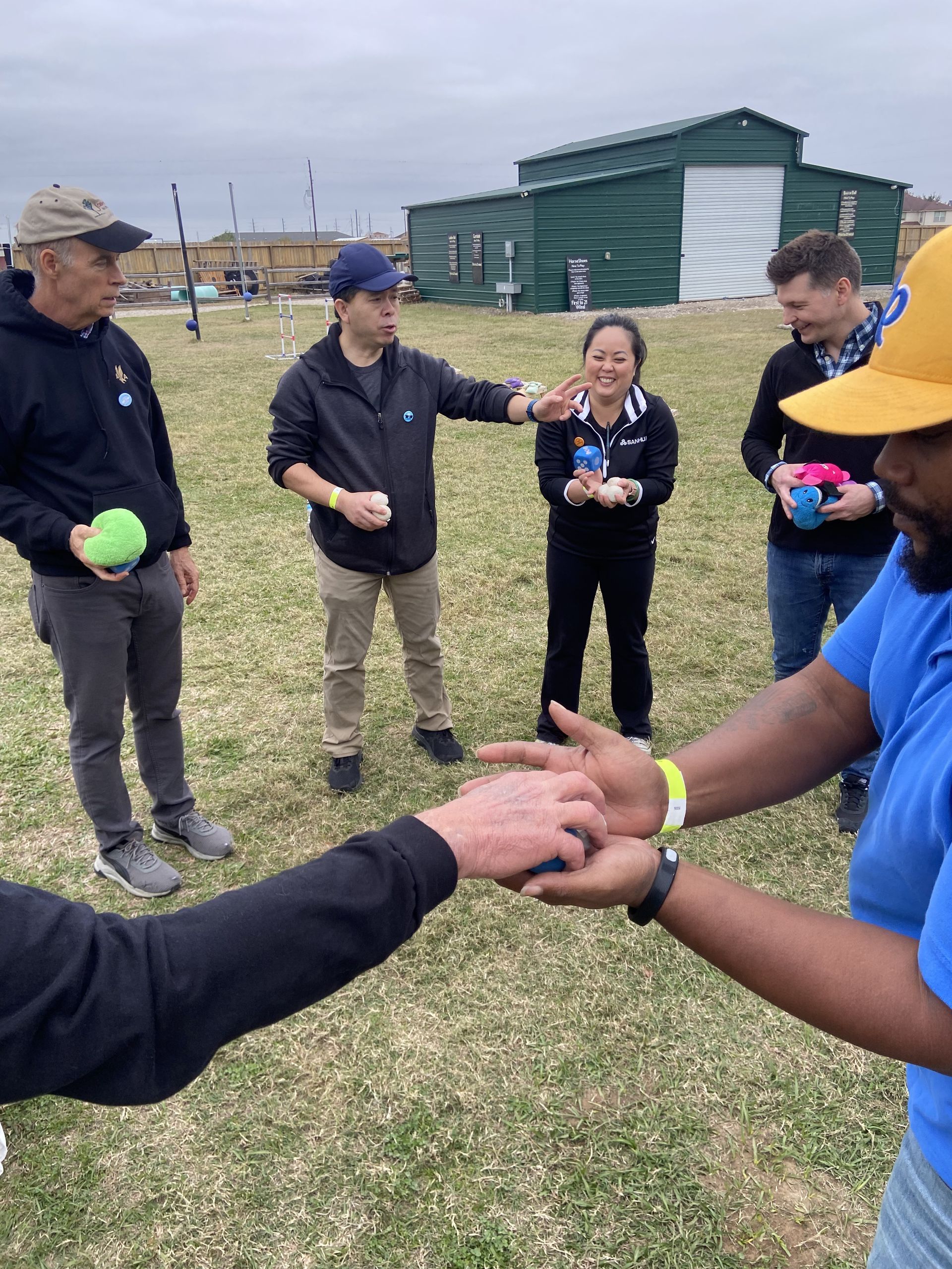 People stacking hands in a grassy field, with others standing nearby holding colorful balls.
