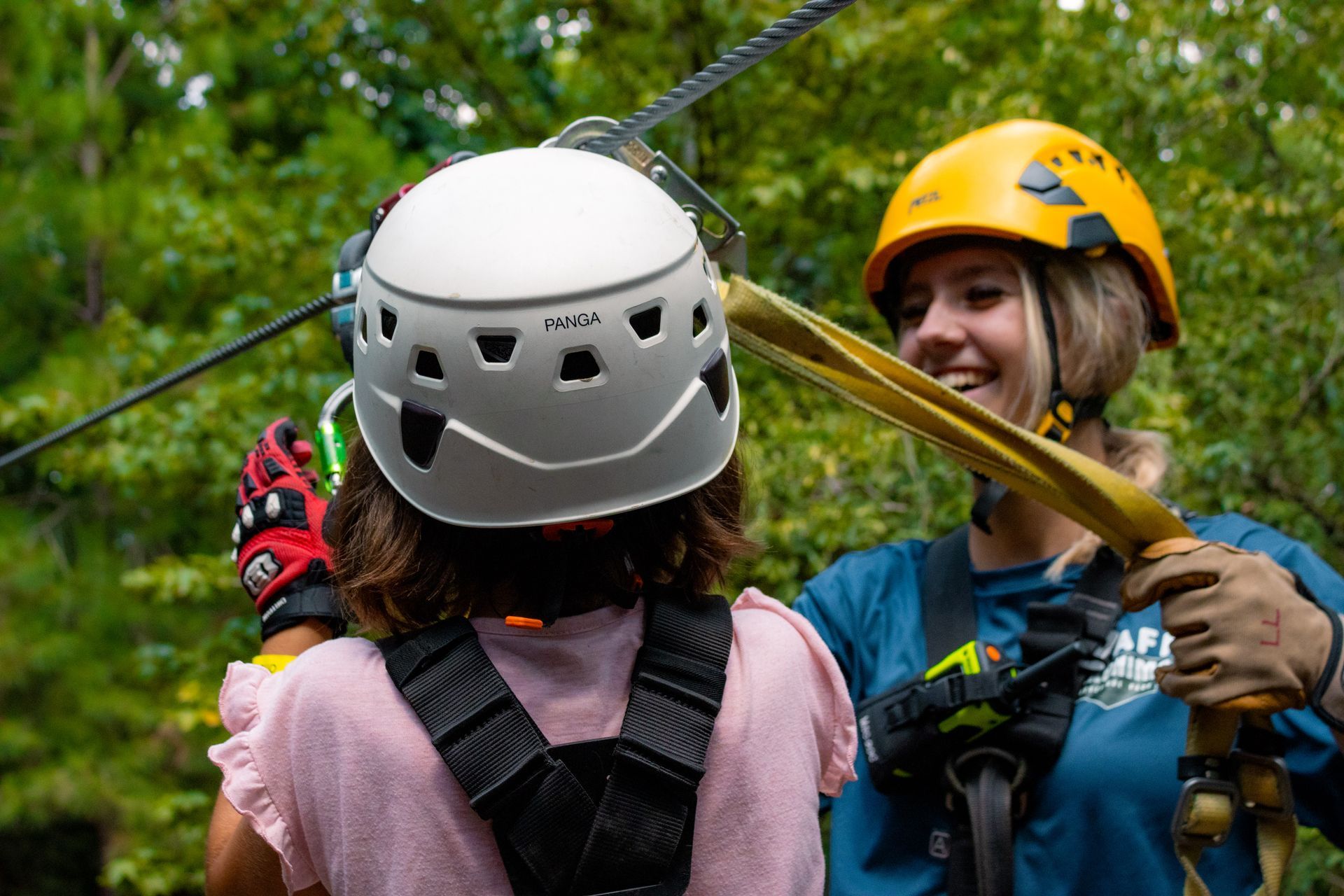 Two climbers in helmets and harnesses smiling on a zip line in a forest canopy