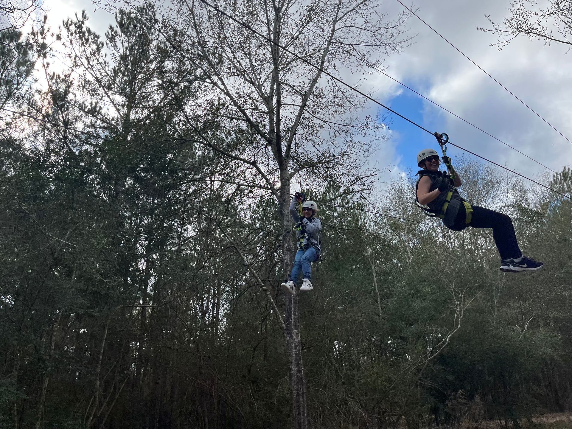 Two people ziplining through a wooded area under a cloudy sky