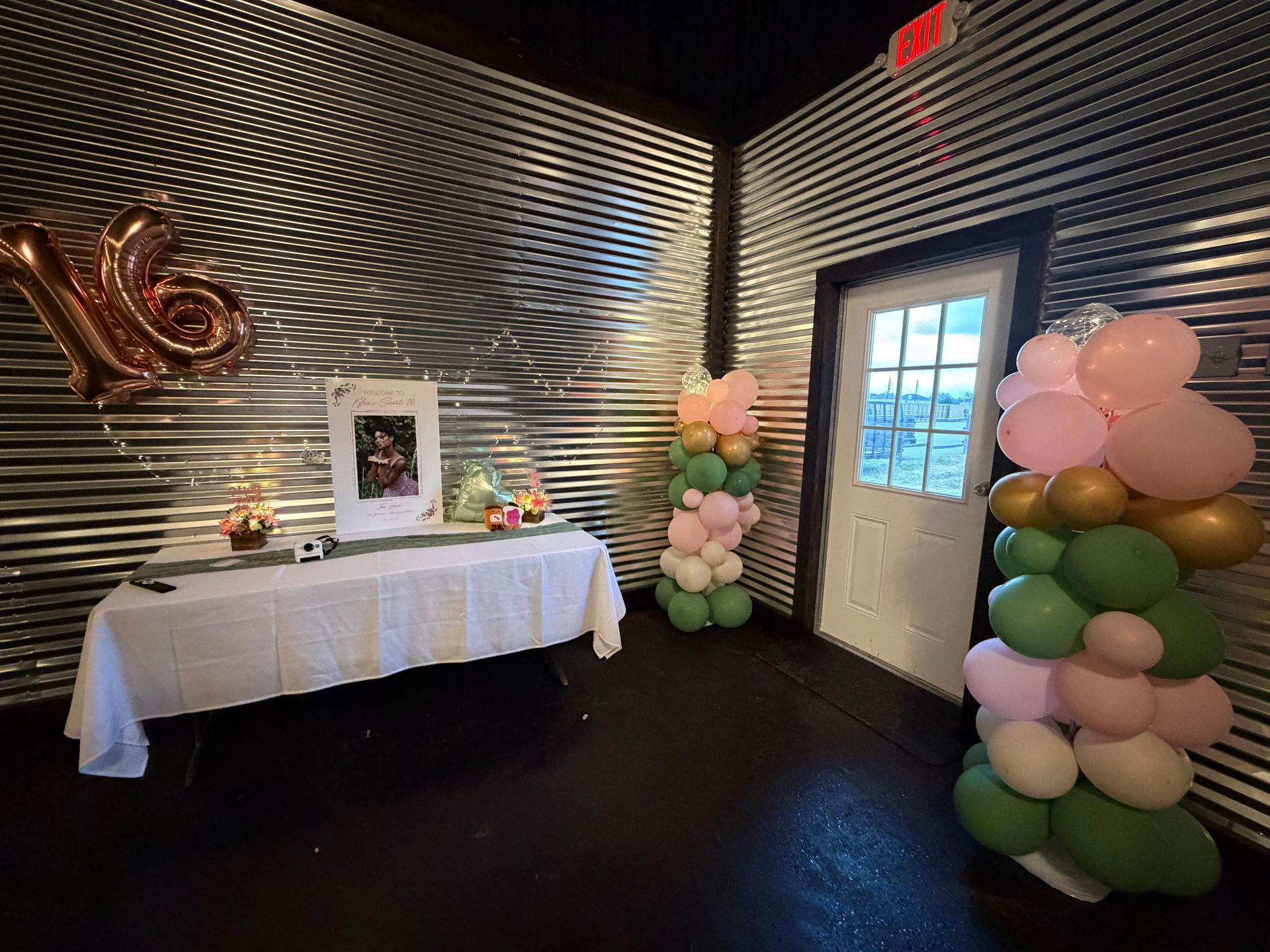 Memorial setup with white table, framed photo, candles, and pastel balloon columns in a decorated room