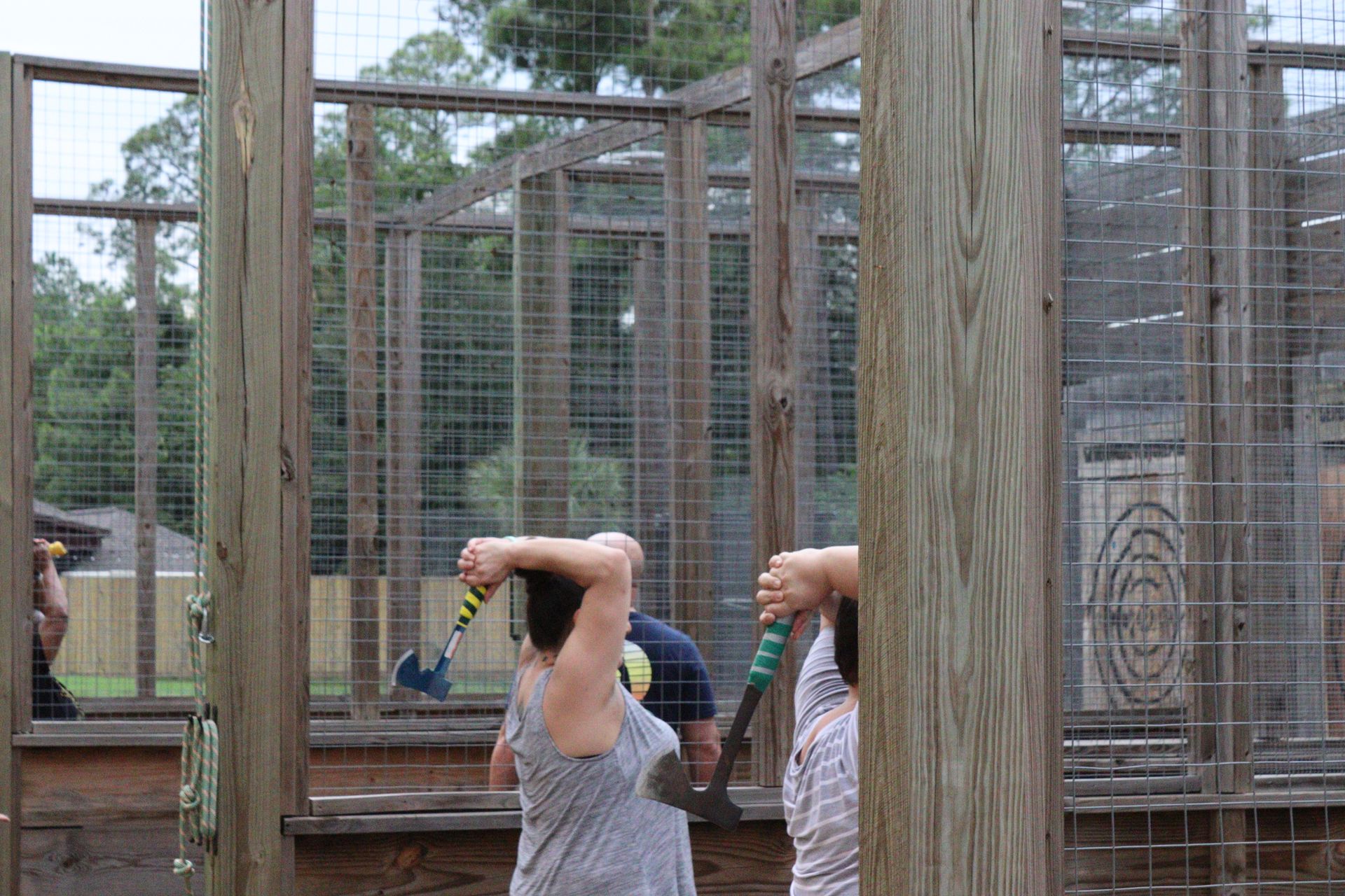 Two people in striped shirts holding tools inside a wooden animal enclosure with wire fencing.
