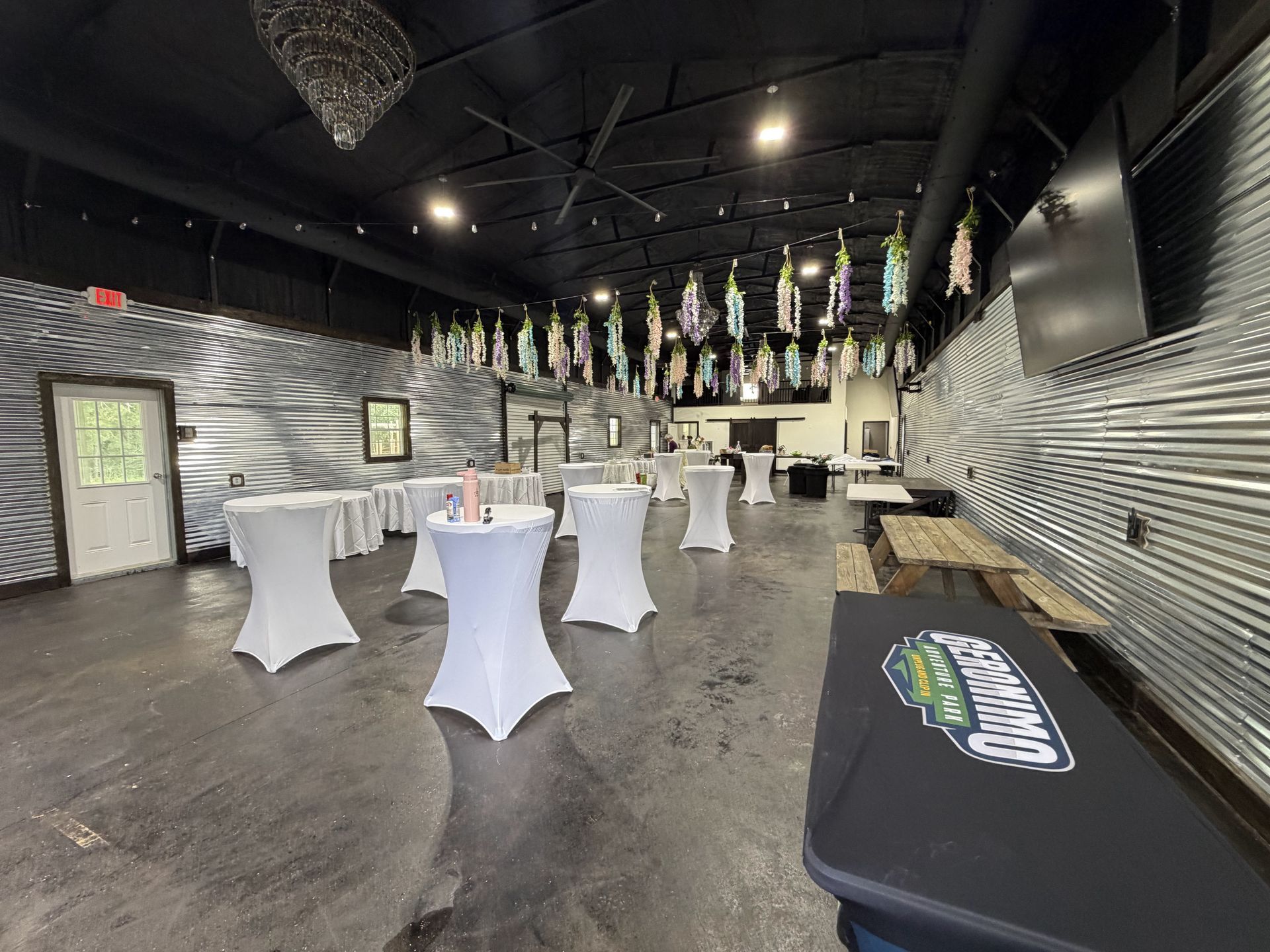 Empty event hall with white cocktail tables, black ceiling, and a lit bar area