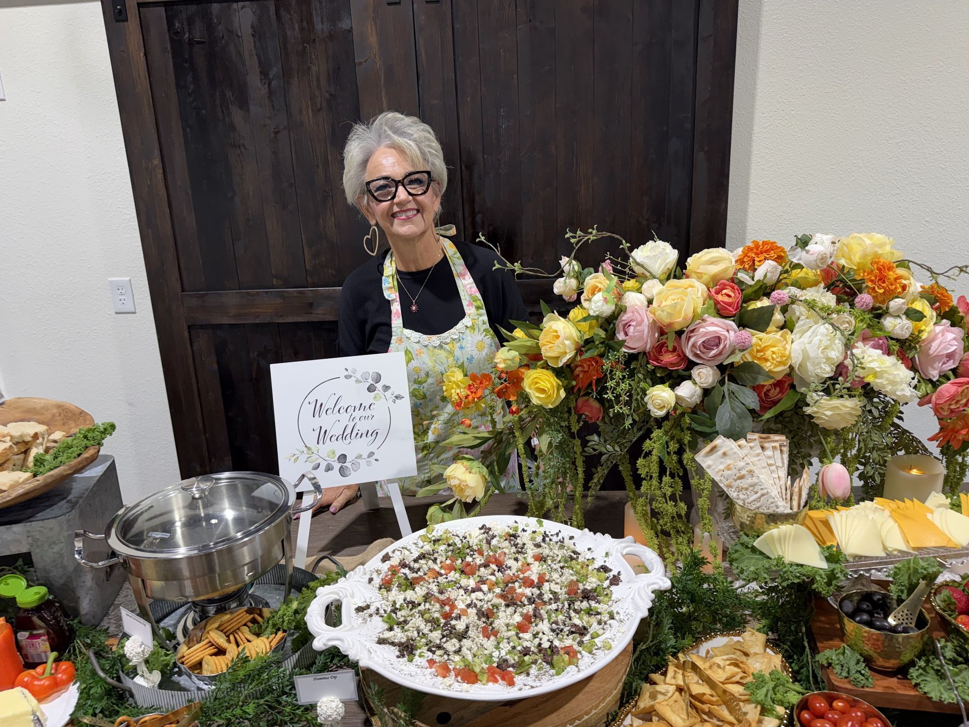 Woman smiling behind a buffet table with flowers, salad, bread, and serving dishes