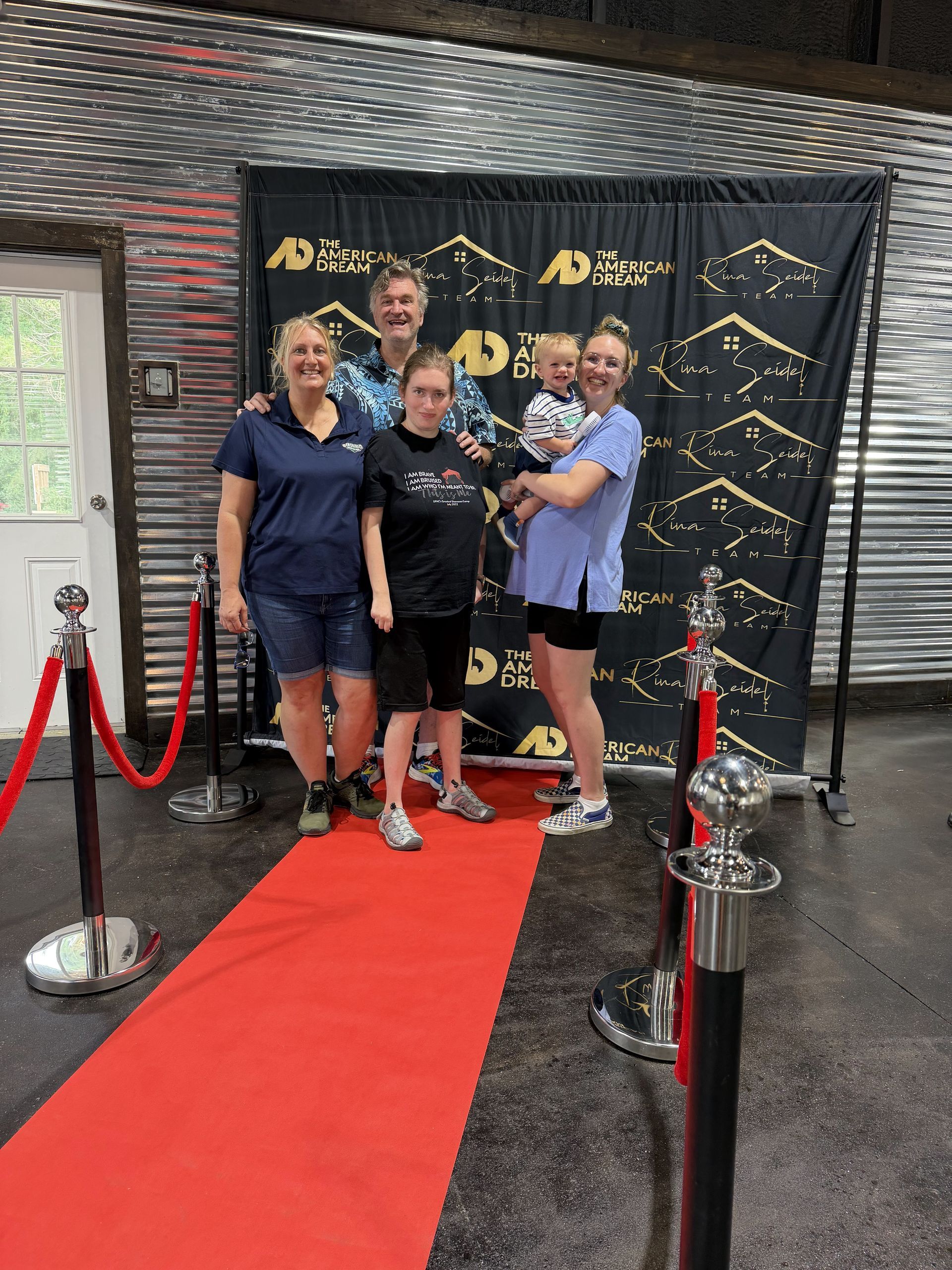 Four people posing on a red carpet in front of a black-and-gold event backdrop