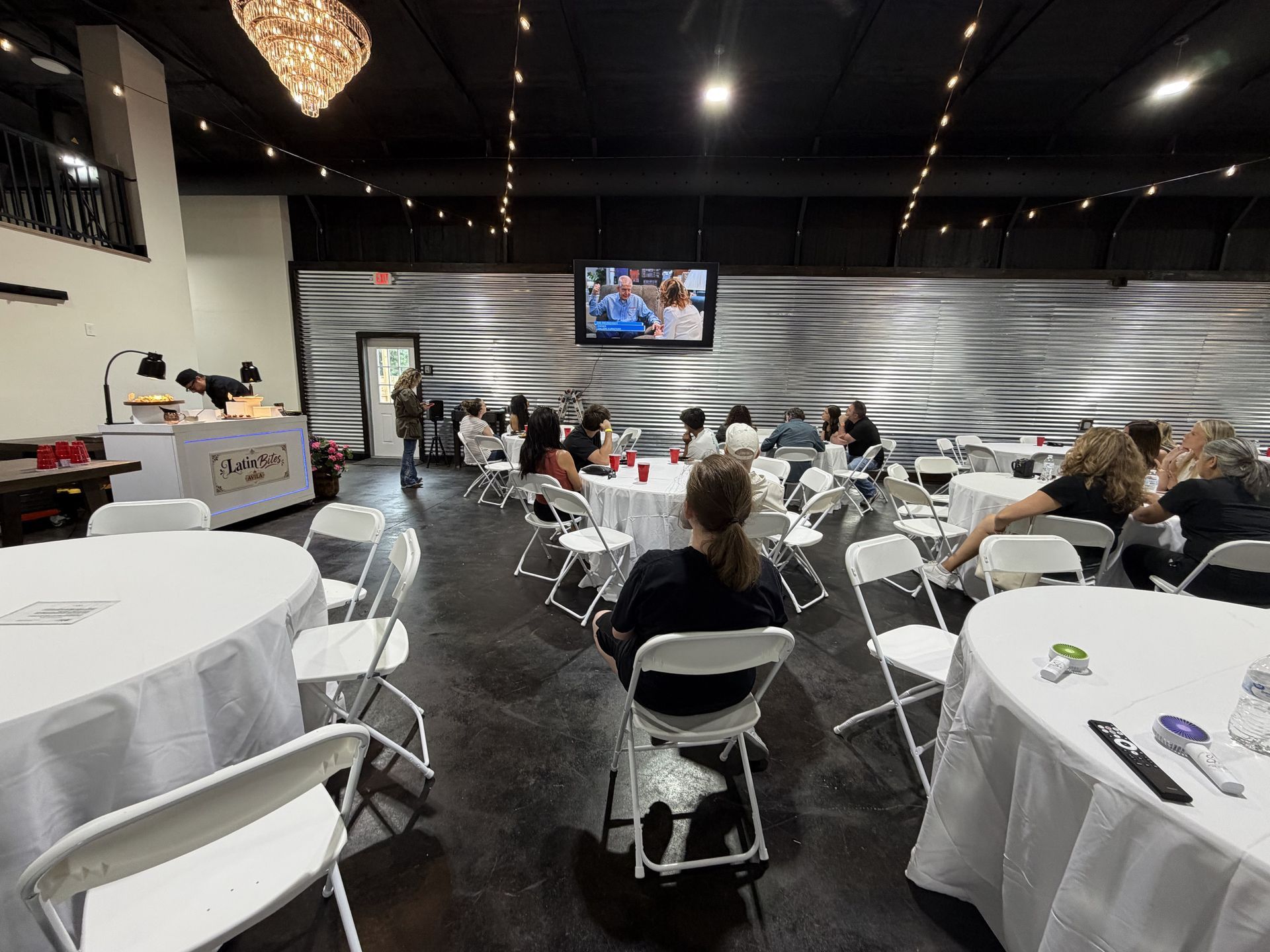 Small event hall with seated guests facing a TV screen at the front.