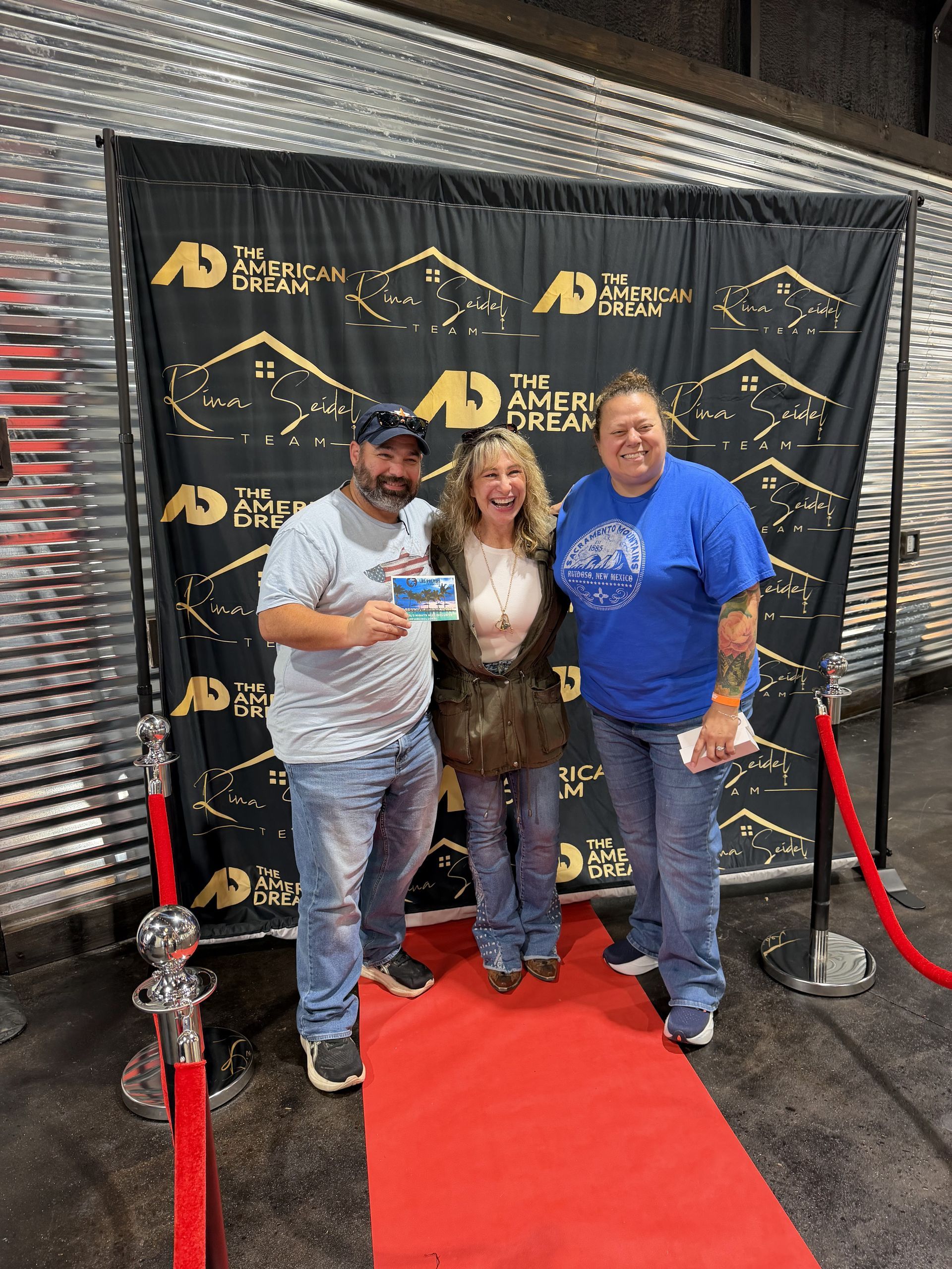 Three people posing on a red carpet in front of a black-and-gold step-and-repeat backdrop