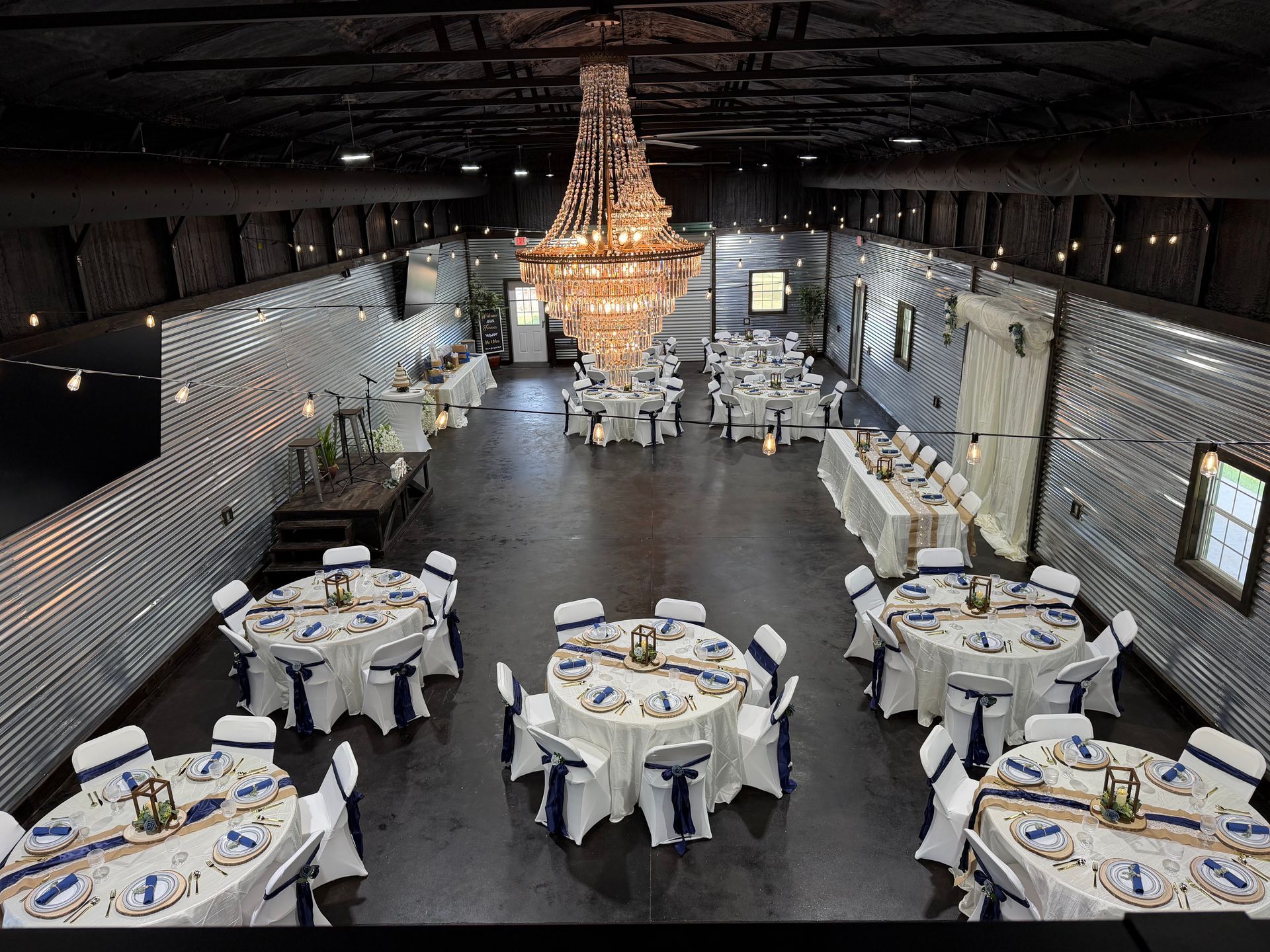Banquet hall with round tables and a large crystal chandelier under a dark ceiling