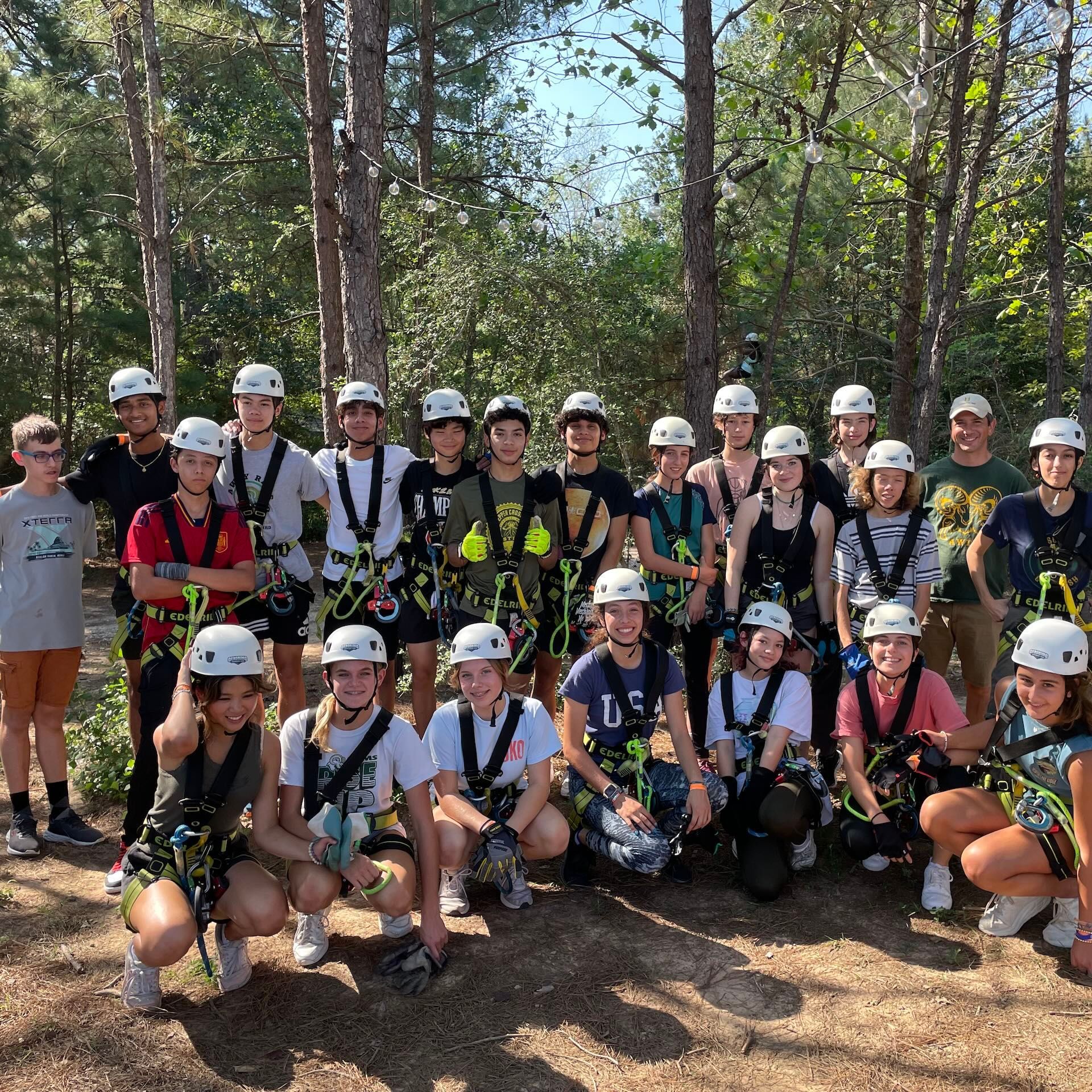 Group of helmeted people posing on zipline gear in a wooded outdoor setting