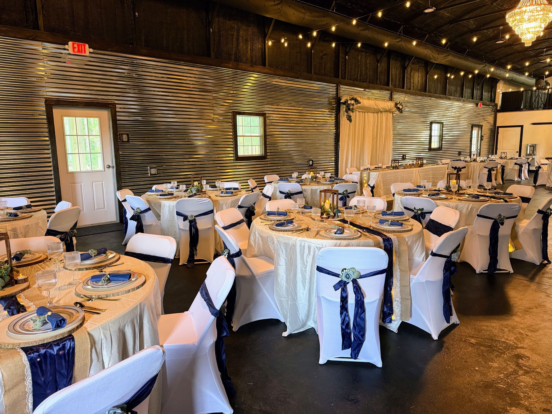 Decorated banquet hall with round tables, white chairs, and blue sashes set for an event