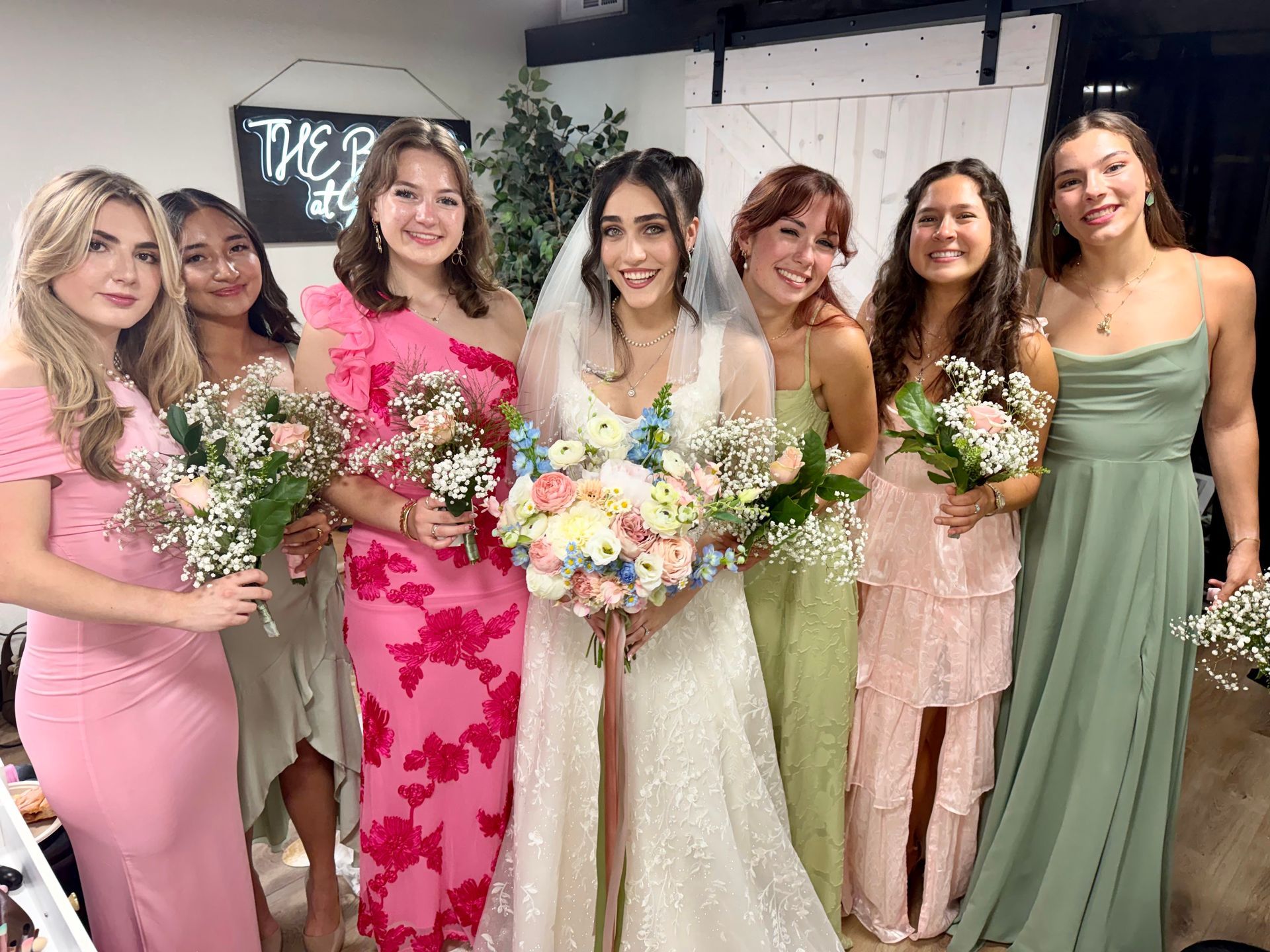 Six women in formal dresses holding colorful bouquets at a wedding or bridal shower.