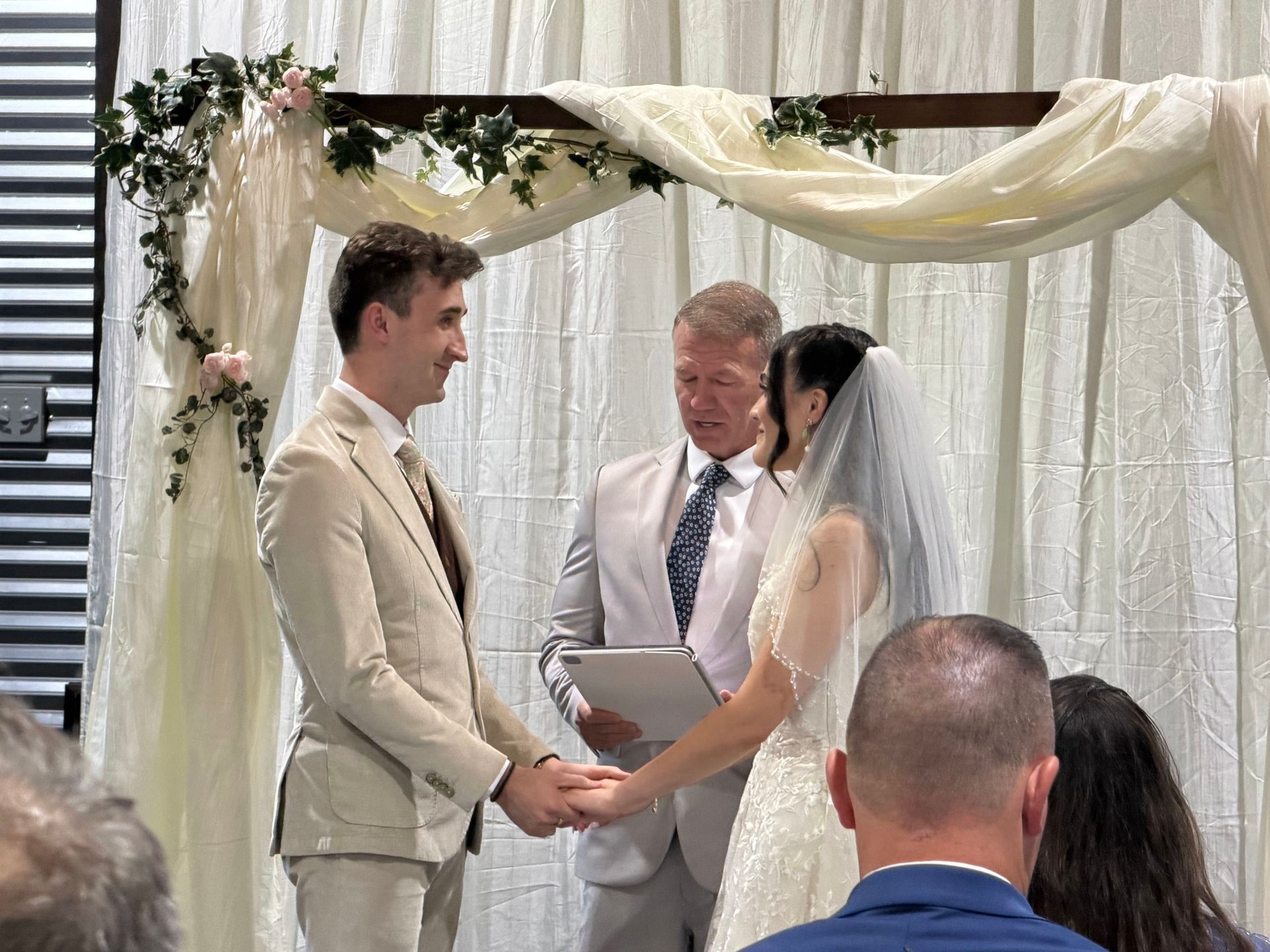 Wedding couple exchanging vows under a decorated arch with officiant holding a folder