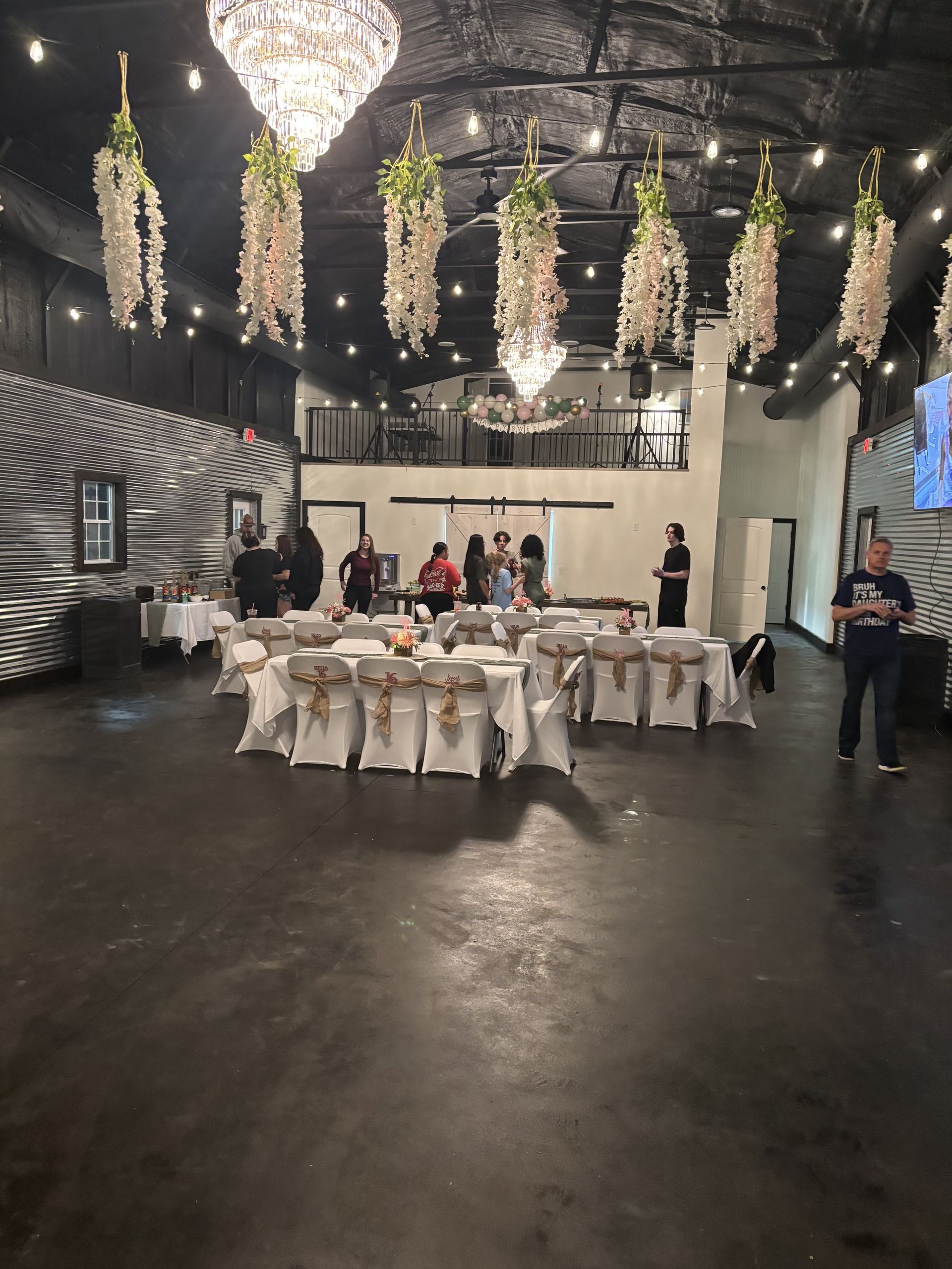 Banquet hall with white-draped tables, chandeliers, and hanging greenery decorations.