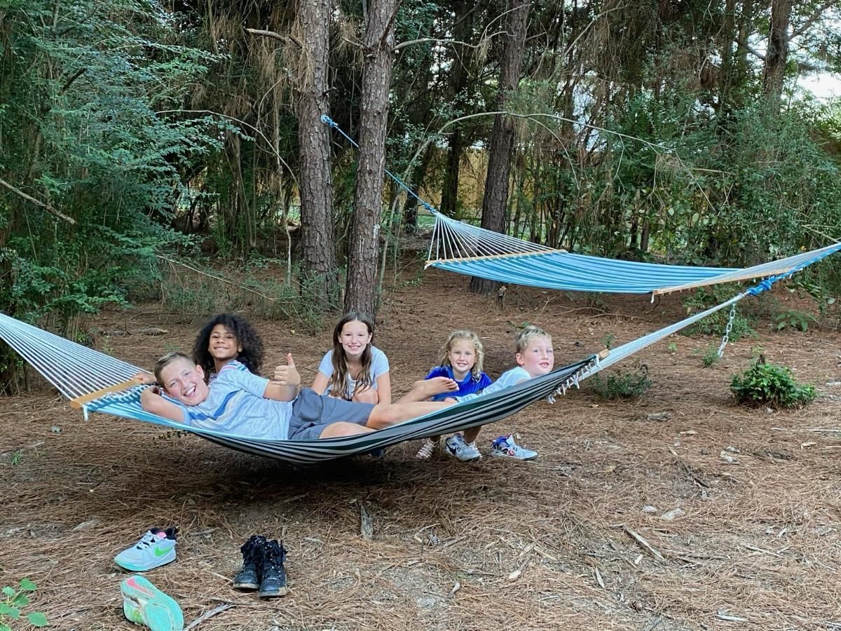 Five children relaxing together in a hammock in a wooded campsite