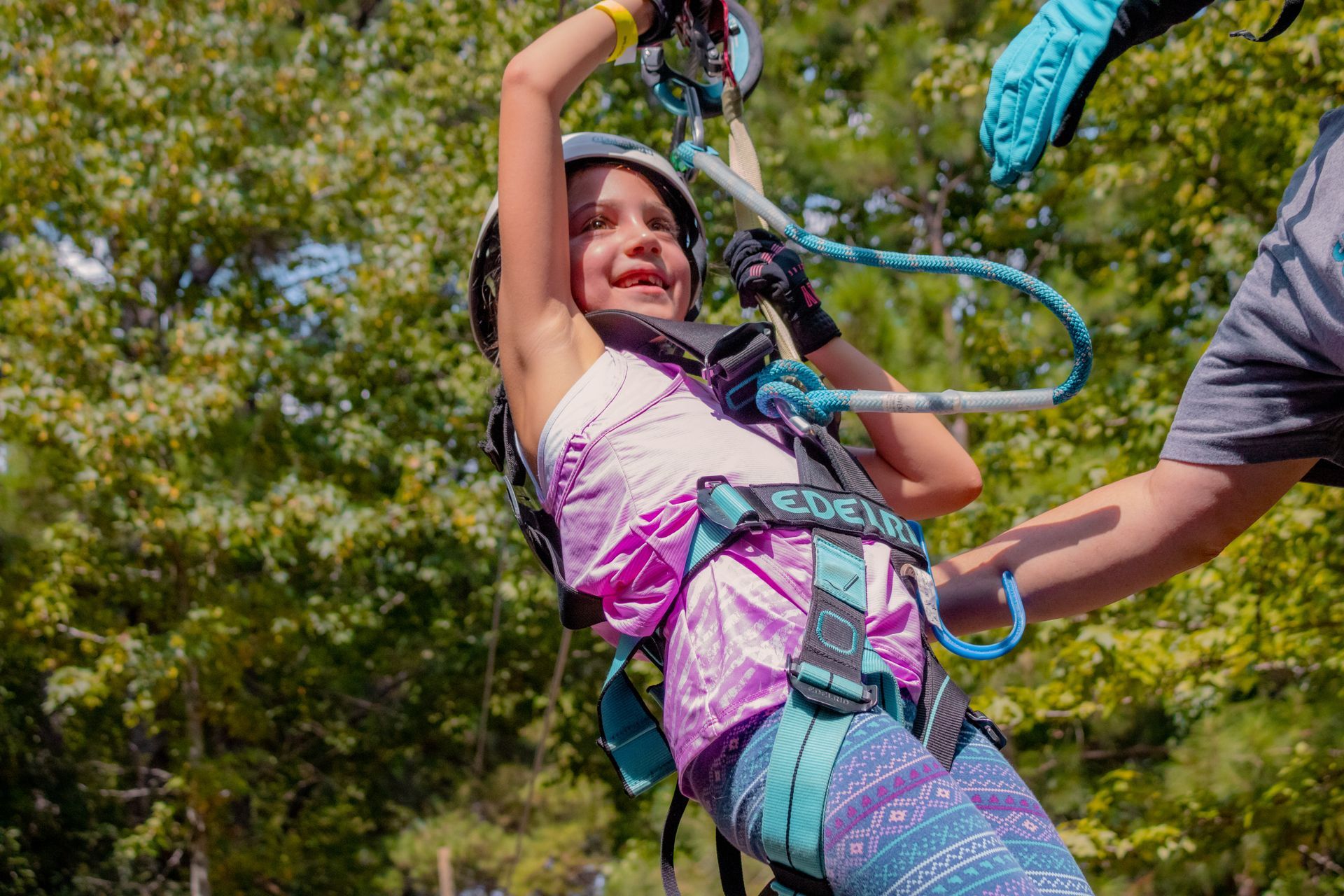 Child zip-lining outdoors, smiling and holding the harness rope amid trees