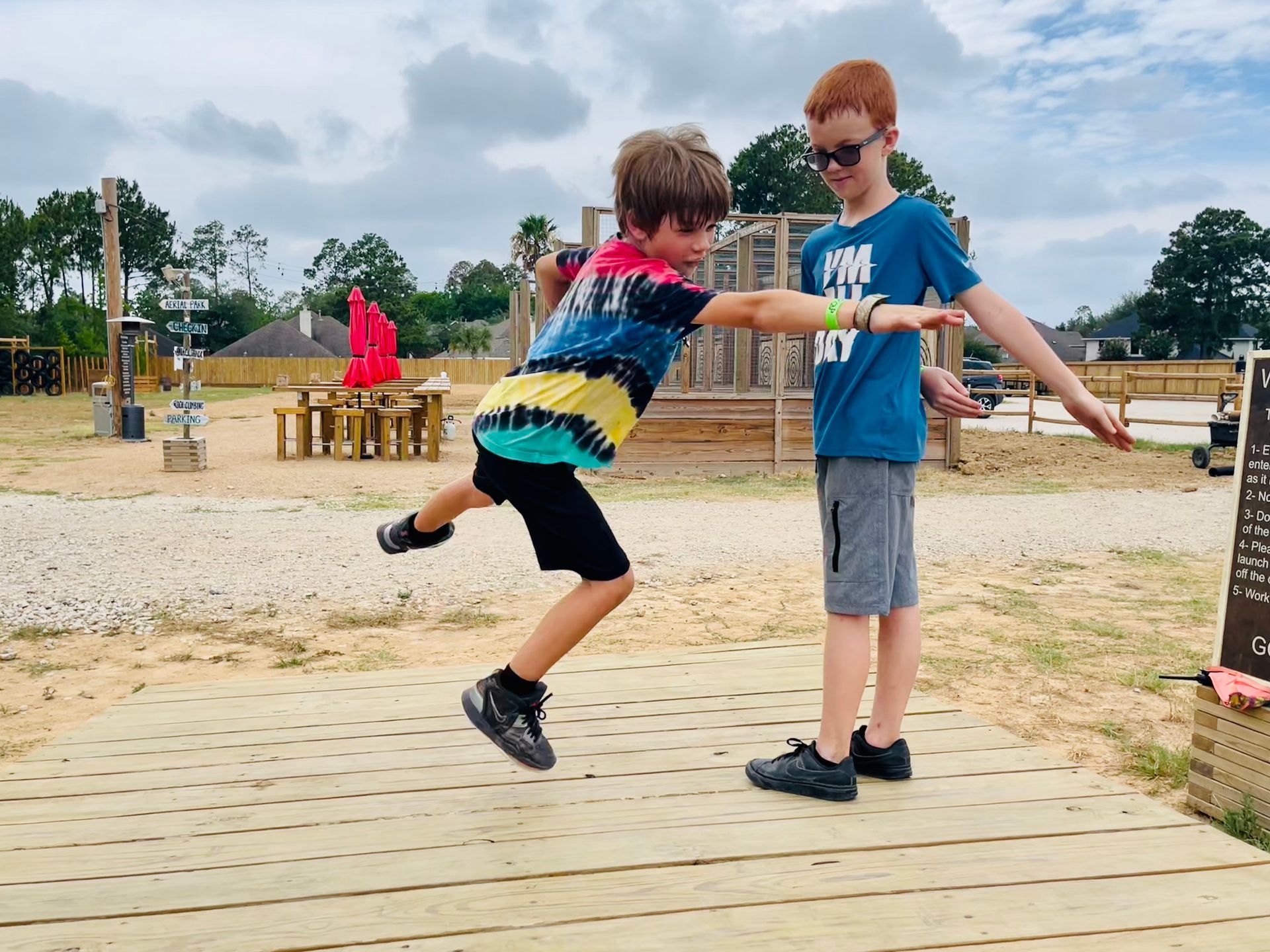 Two children on a wooden platform playfully reaching toward each other in a park