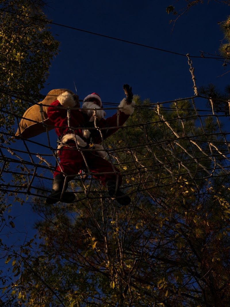 Santa in red climbing a rope net obstacle at night among trees