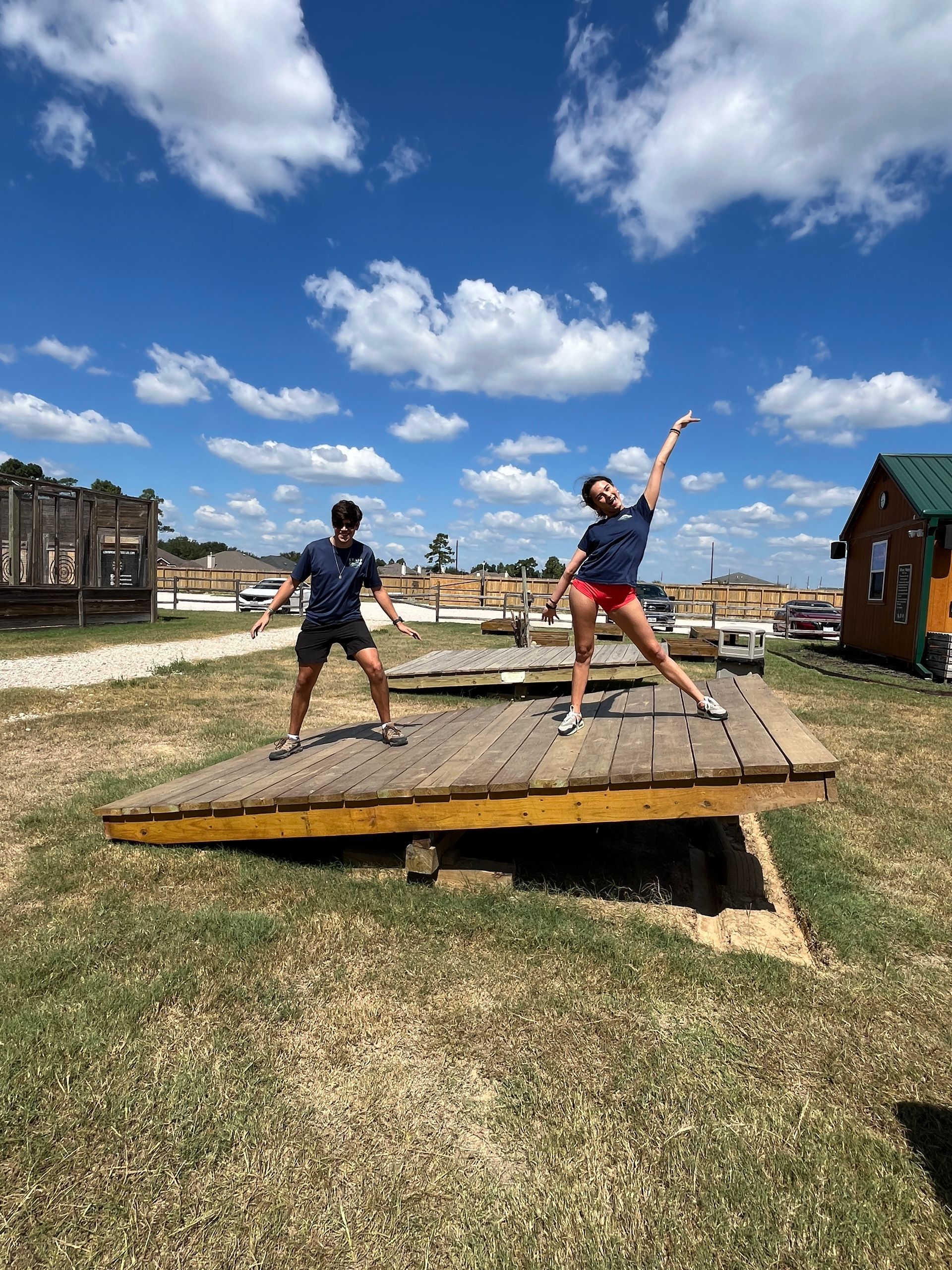 Two people balancing on a seesaw outdoors under a blue sky with clouds