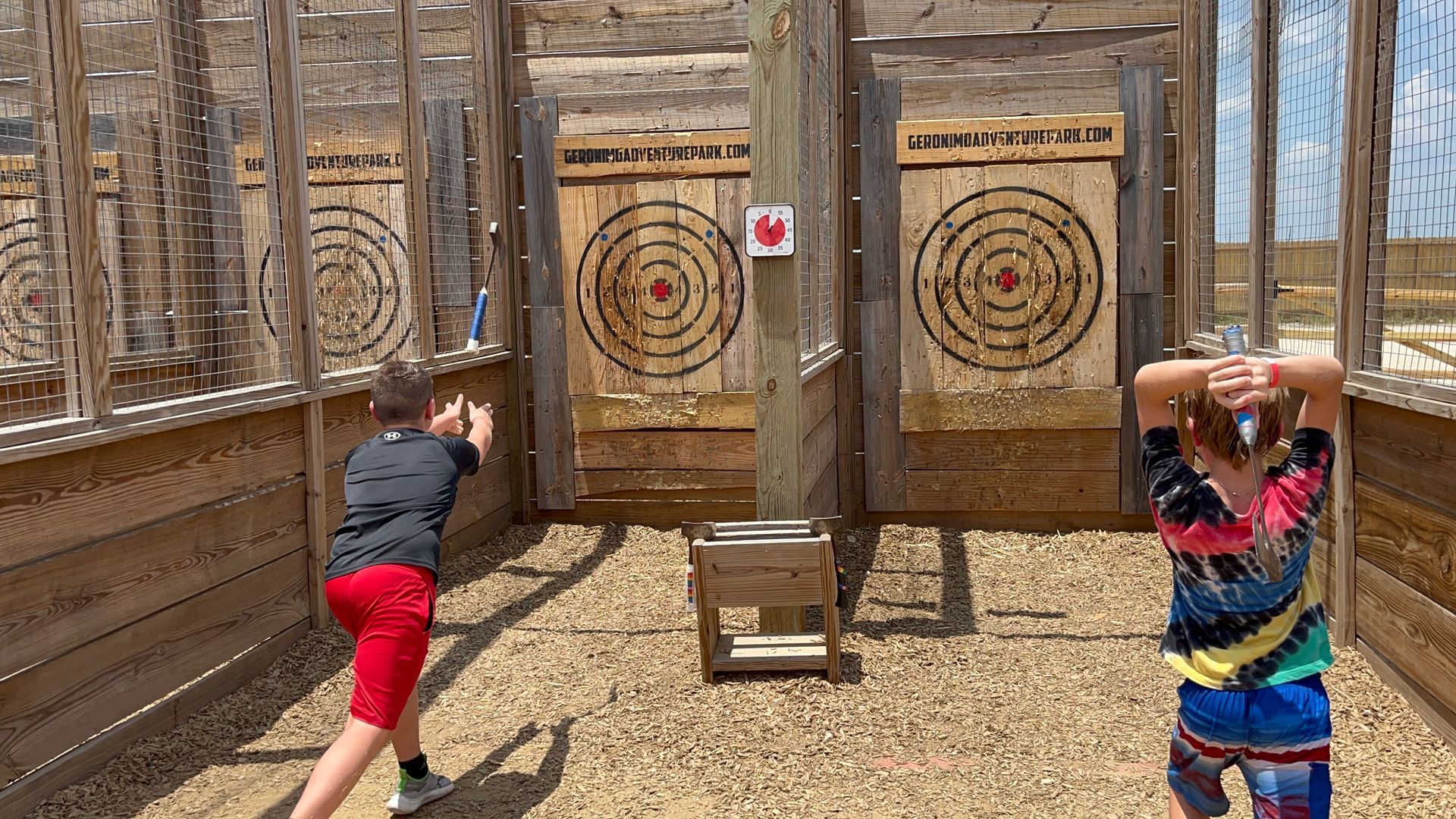 Two people throwing axes at targets in an outdoor wooden range