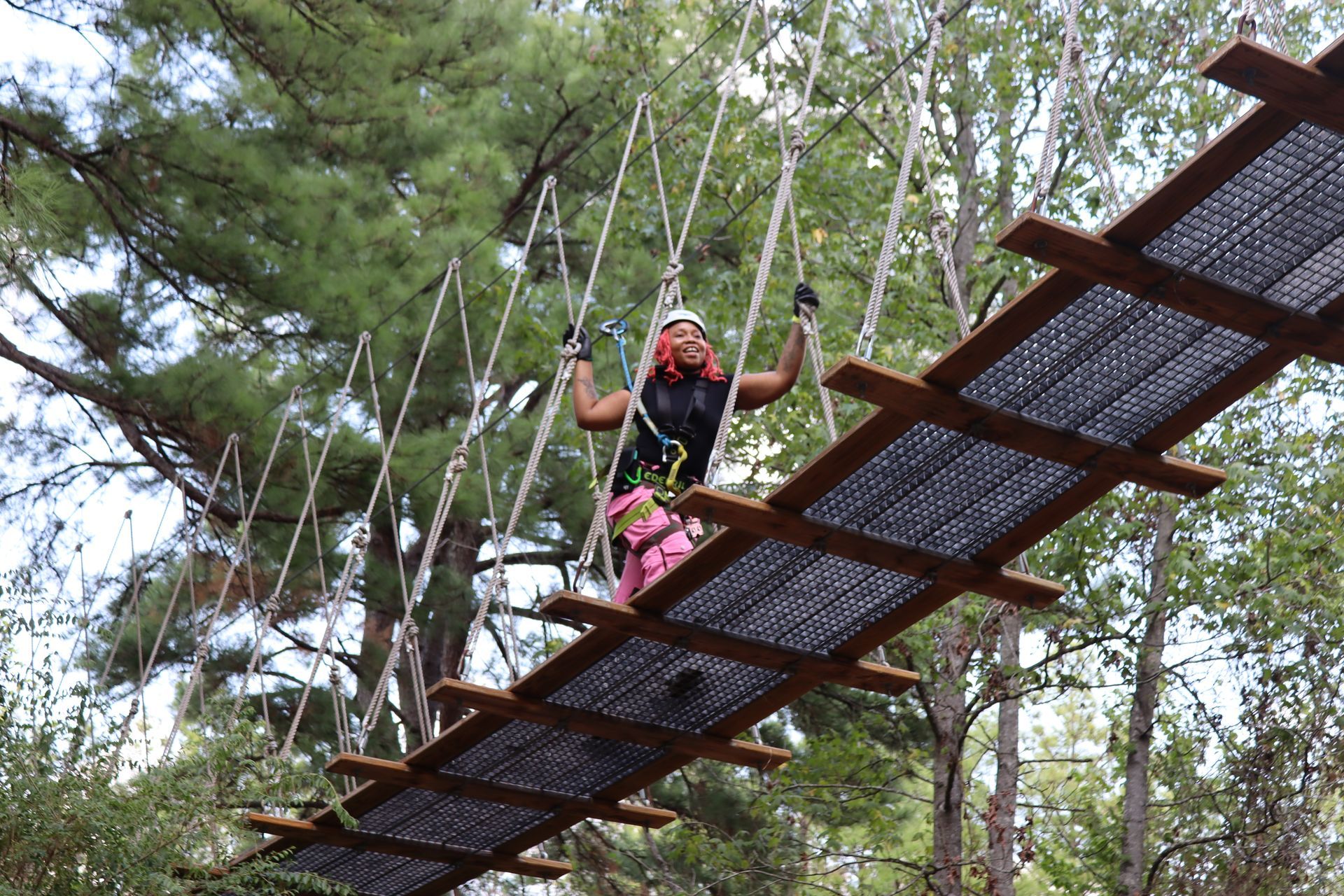 Person crossing a rope bridge in a wooded outdoor adventure course