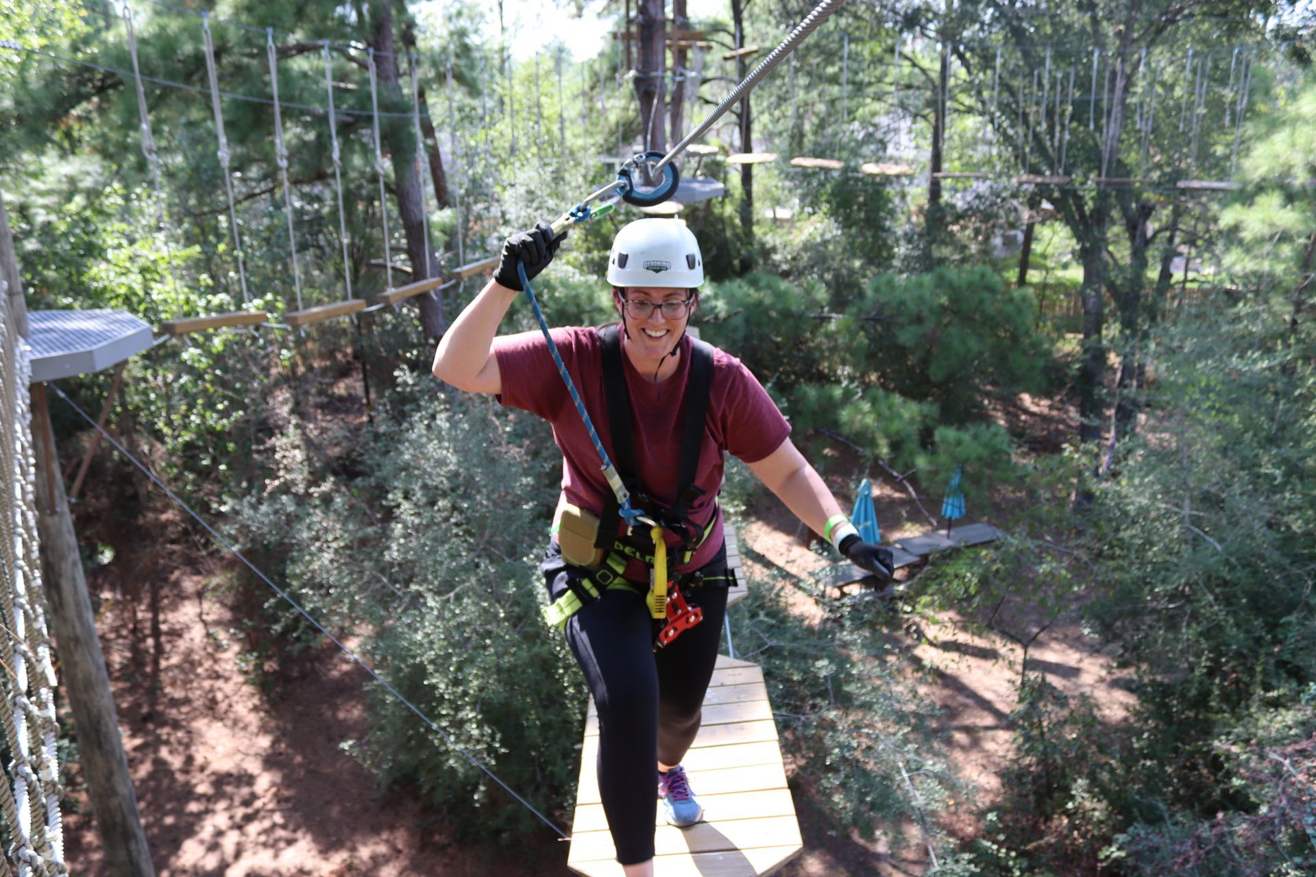 Person in a helmet and harness crosses a rope bridge in a forest adventure course