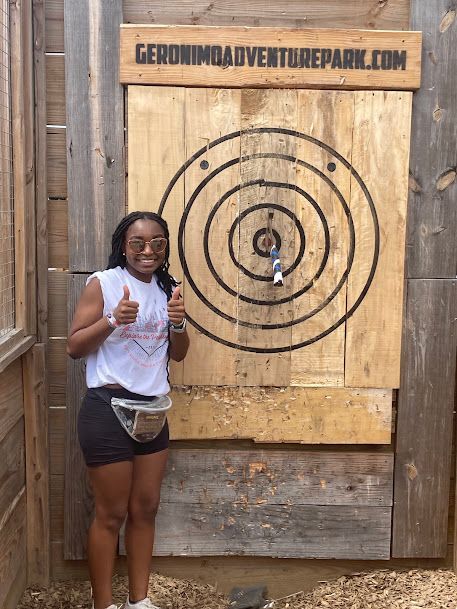 Person smiling and giving a thumbs-up beside a target board at a carnival game booth.