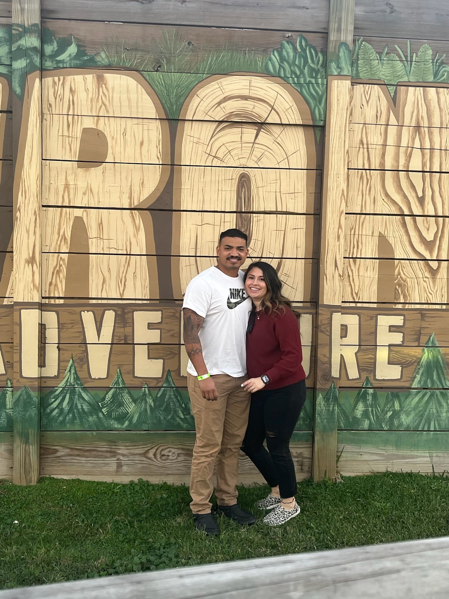 Couple posing in front of a wooden “LOVE” sign outdoors at a park.