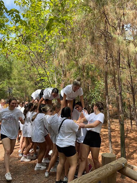 Group of people in white shirts carrying teammates outdoors on a wooded trail