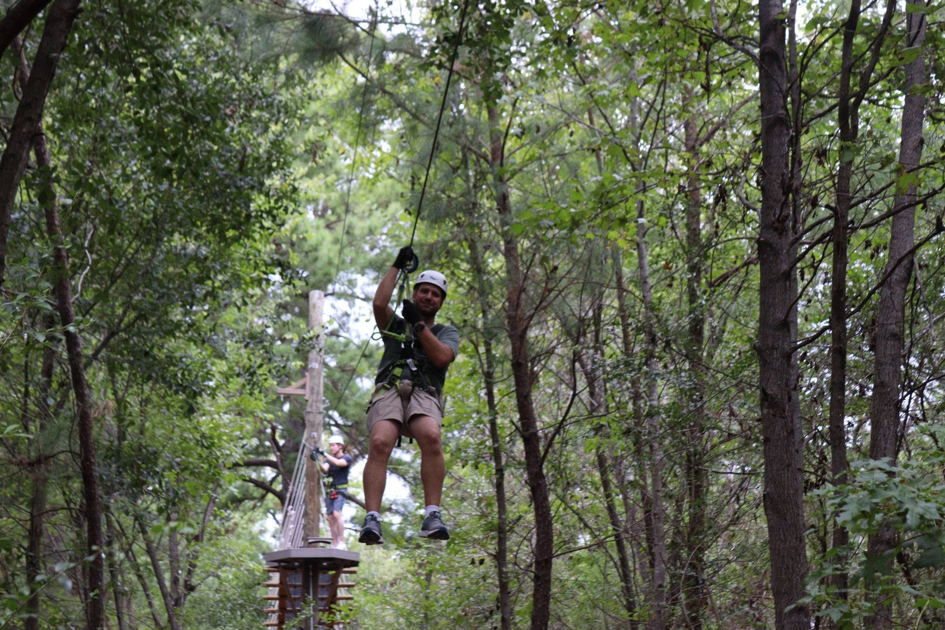 Person ziplining through a wooded forest, wearing a helmet and harness.